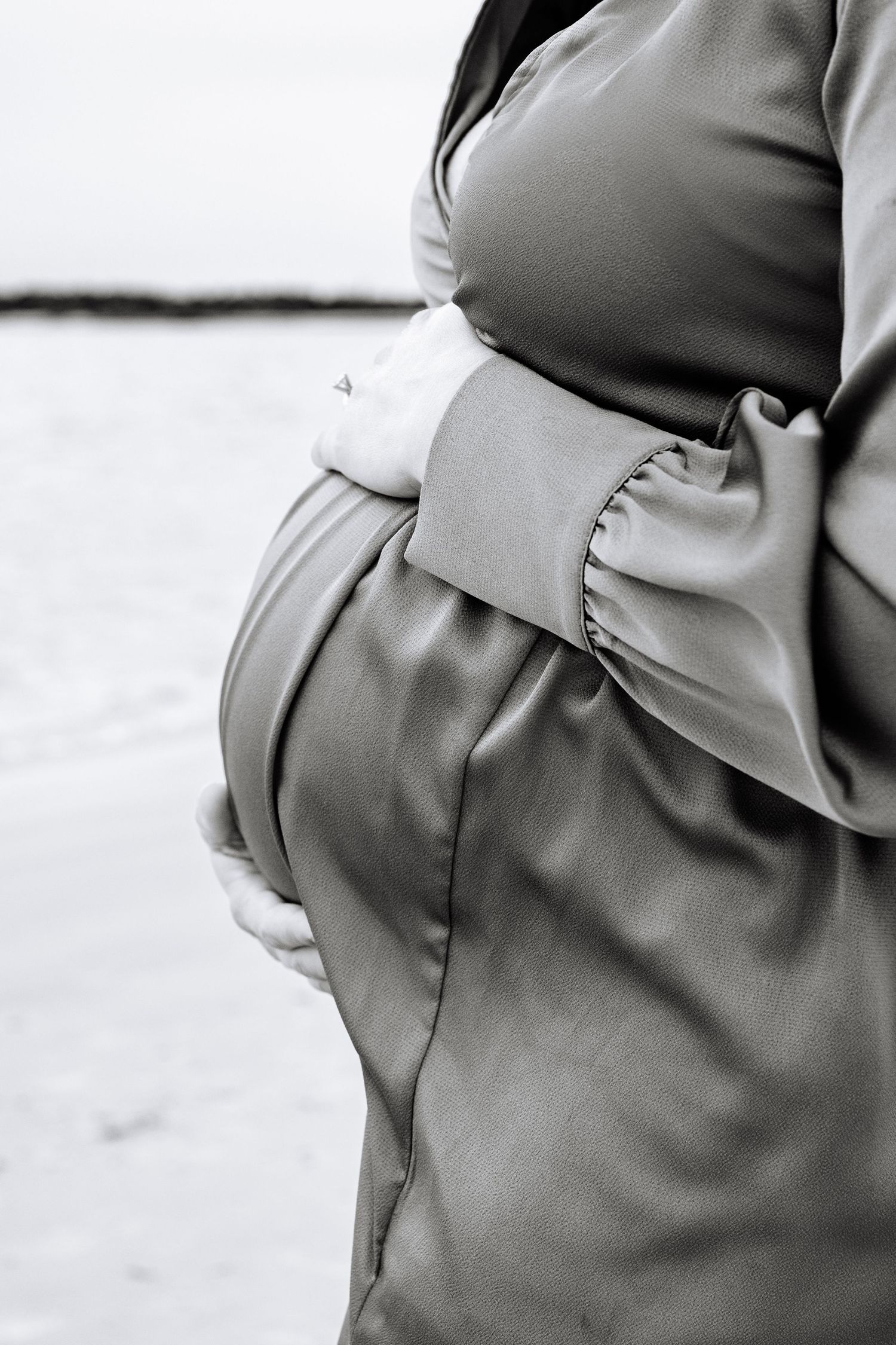 Black and white side view of pregnant woman's belly in elegant dress showing maternity curves and hand placement.