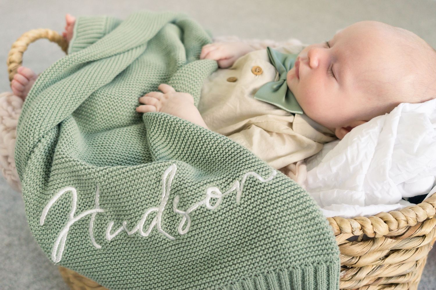 Baby sleeps peacefully with mint green knitted blanket personalized with name in white script.