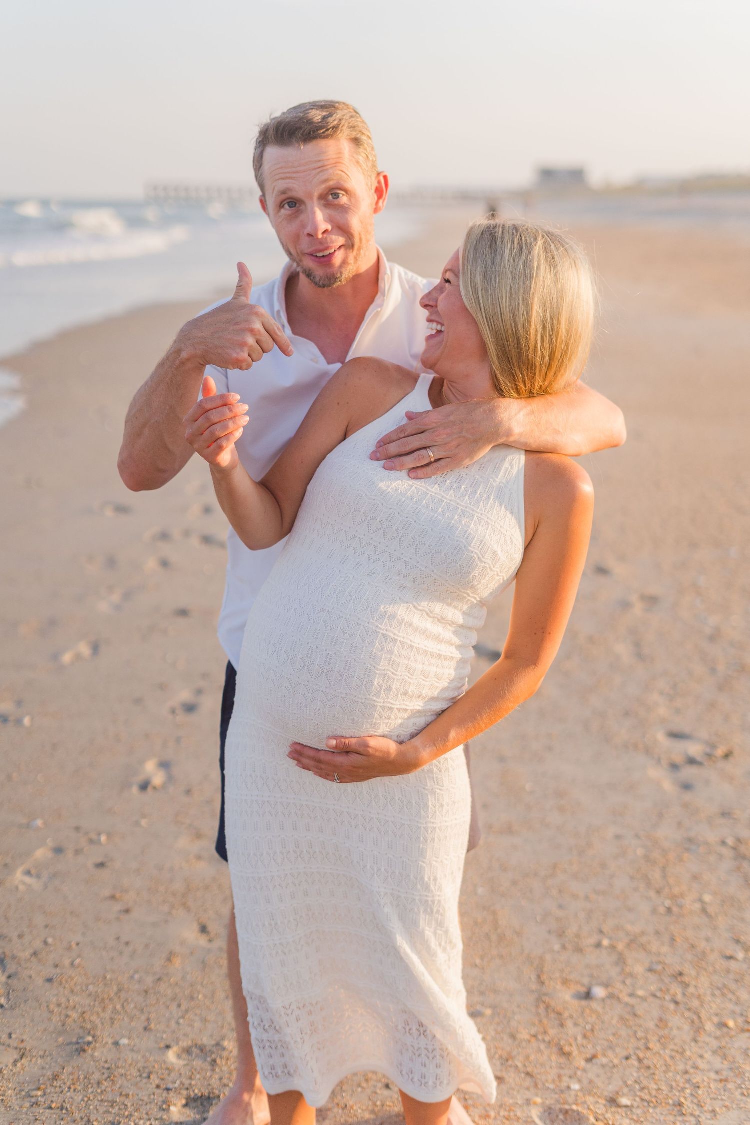 Cheerful couple shows excitement during beachside maternity photoshoot at dusk.