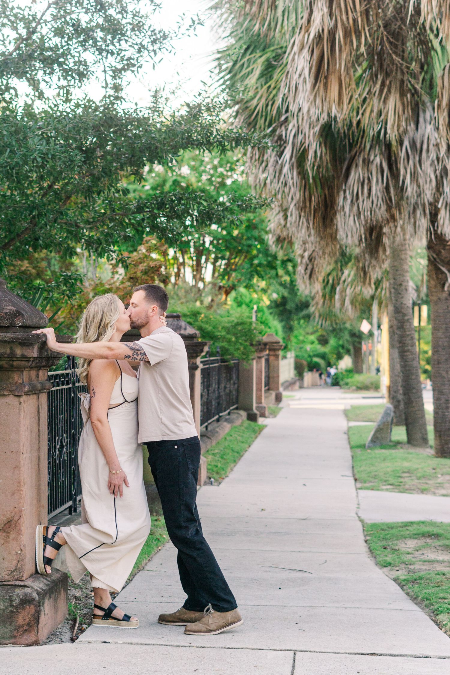 A romantic moment between a couple on a palm tree-lined sidewalk with vintage iron railings.