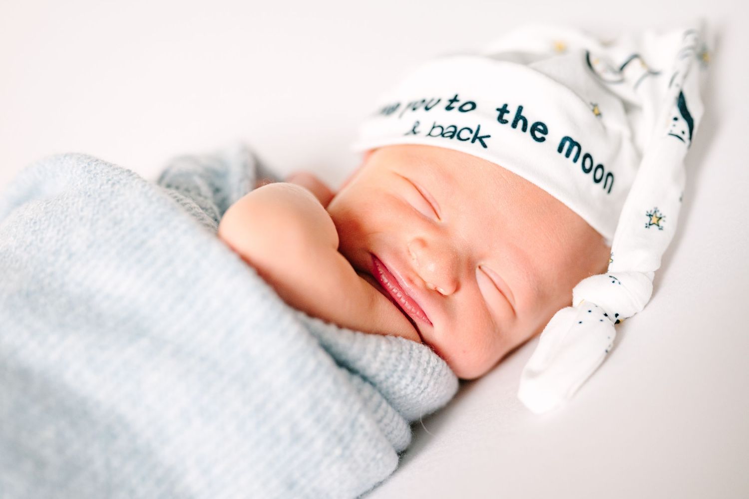 Sleeping newborn in white hat with text and blue blanket against light background.