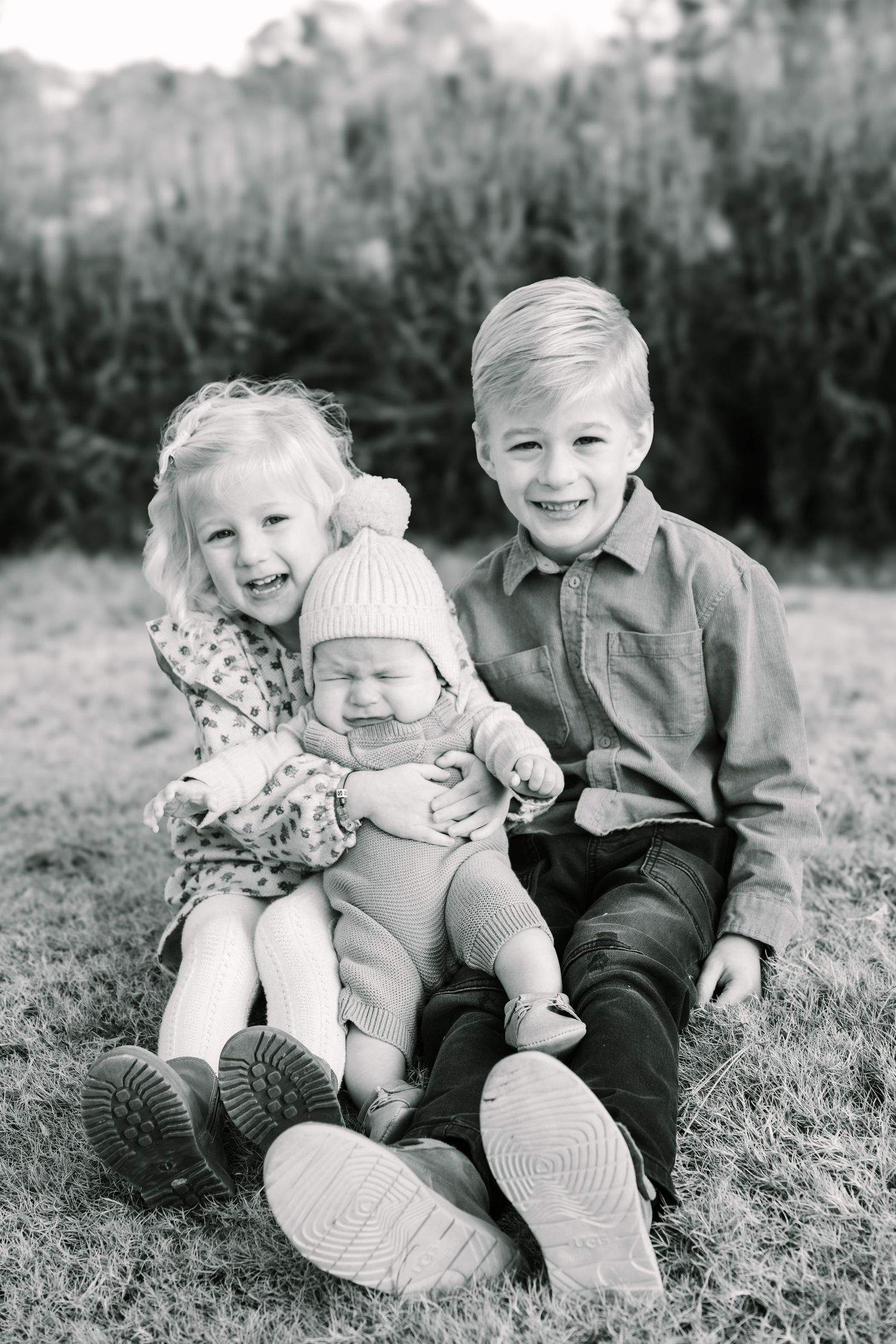 Three children sitting together outdoors for black and white portrait.