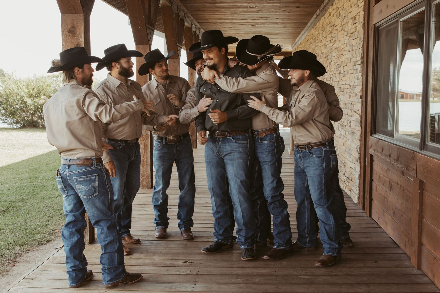 Line of people in western attire standing against brick wall and wooden posts of covered porch. Wedding photographer DFW
