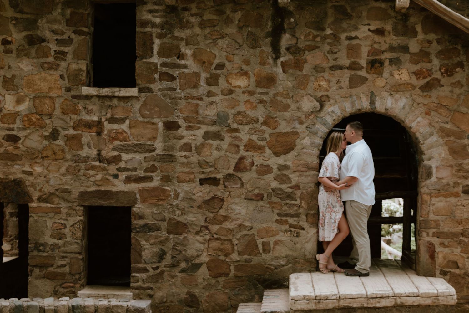 A romantic couple stands in a stone archway of a rustic historic building during their engagement photo session.