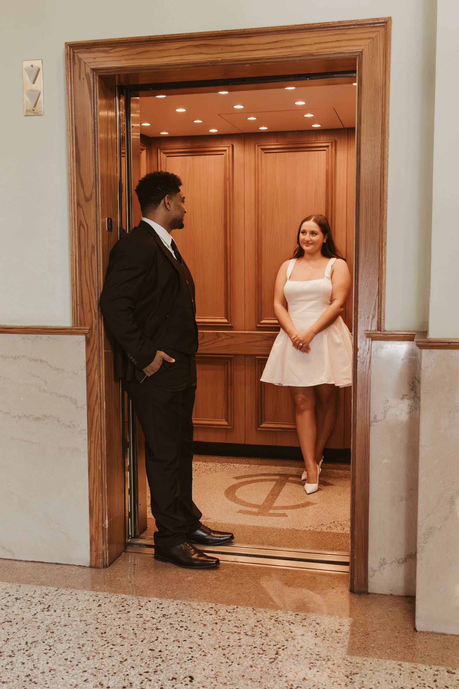 Couple shares a moment by wooden elevator doors in formal attire. Wedding Photographer DFW