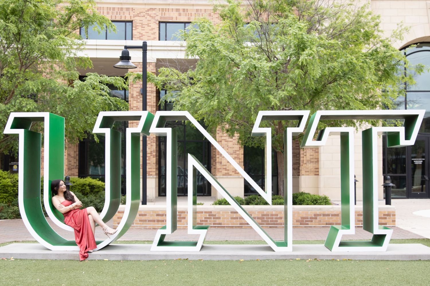 Large green and white UNT university letters displayed as outdoor signage on a landscaped lawn with brick buildings in background.
