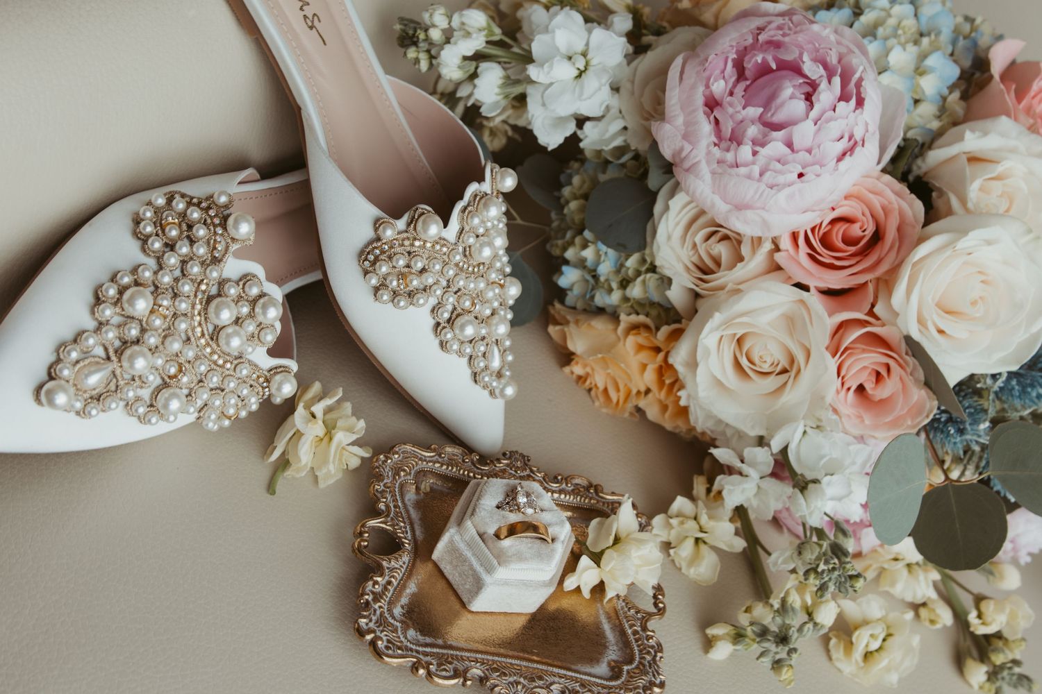 Elegant bridal accessories including sparkly shoes, floral bouquet and jewelry displayed on a vintage tray.