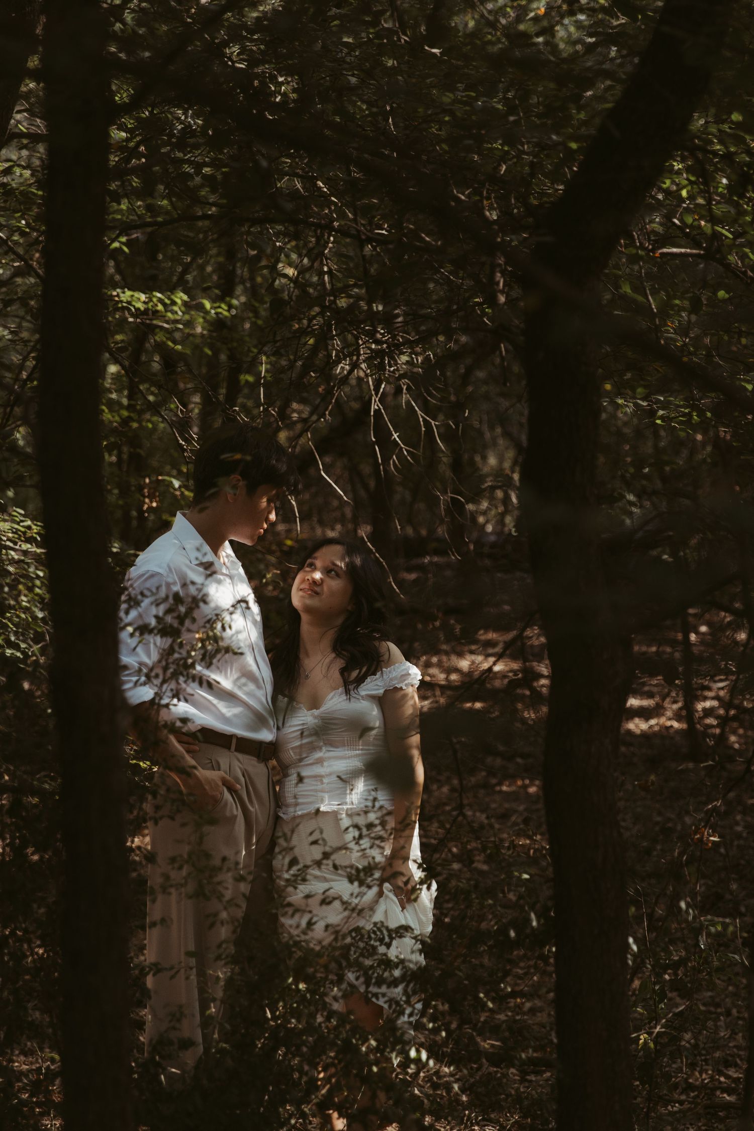 A romantic moment captured in a moody wooded setting with sunlight filtering through the trees.