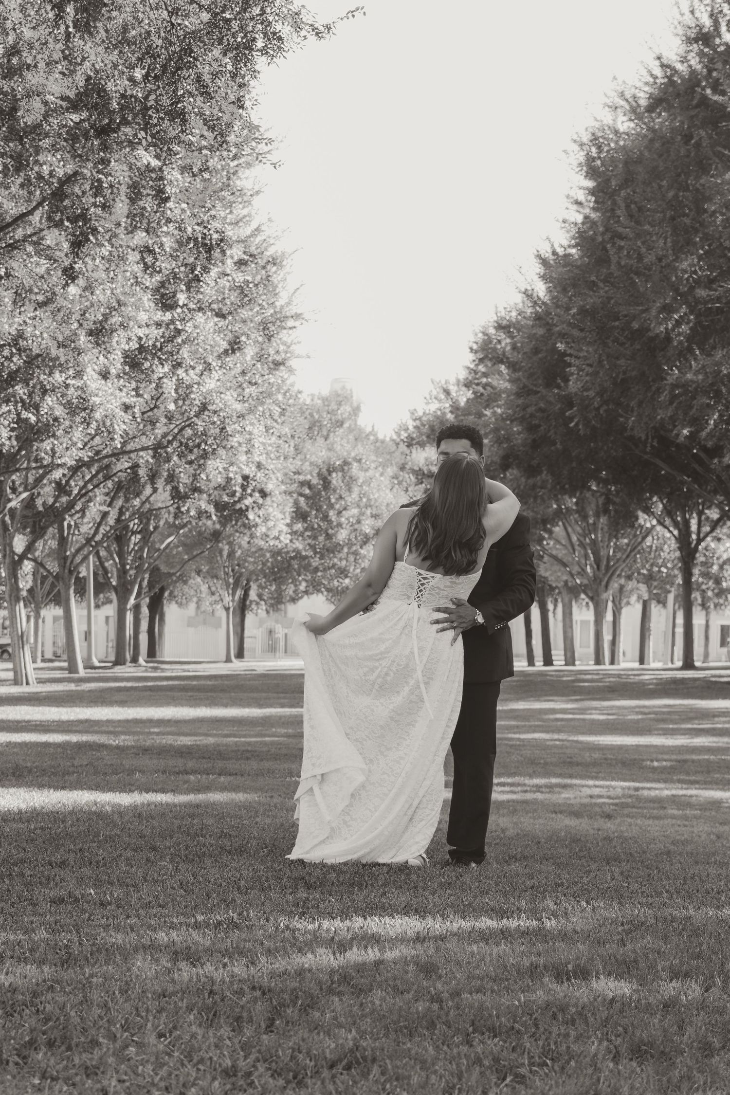 A black and white wedding photo of a couple in a tree-lined outdoor setting. Wedding Photographer DFW