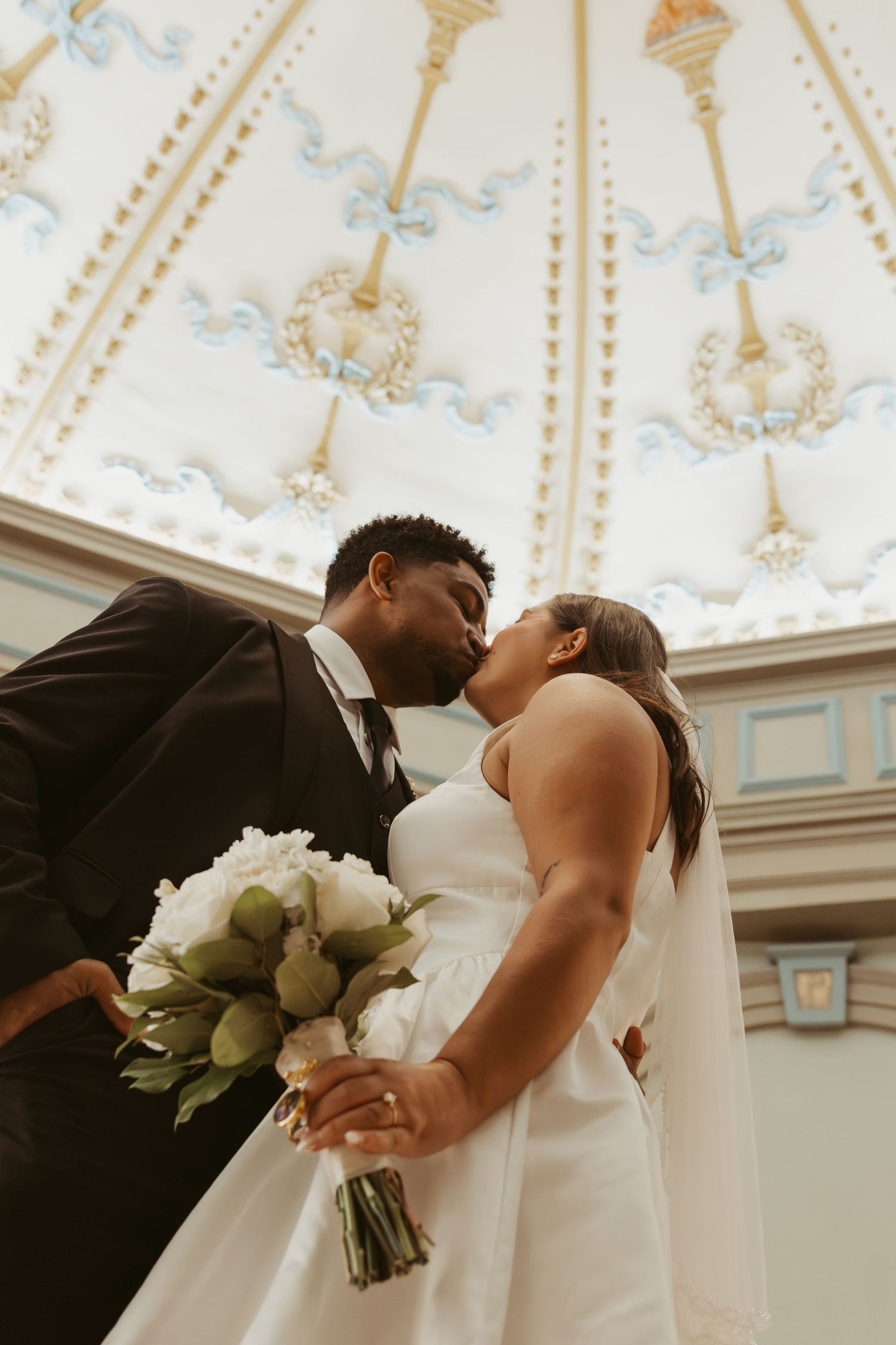 A romantic wedding moment under an ornate white ceiling with decorative details. Wedding Photographer DFW