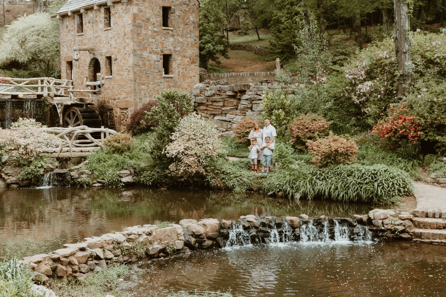 Stone mill and waterfall surrounded by lush gardens and landscaping at a historic site.