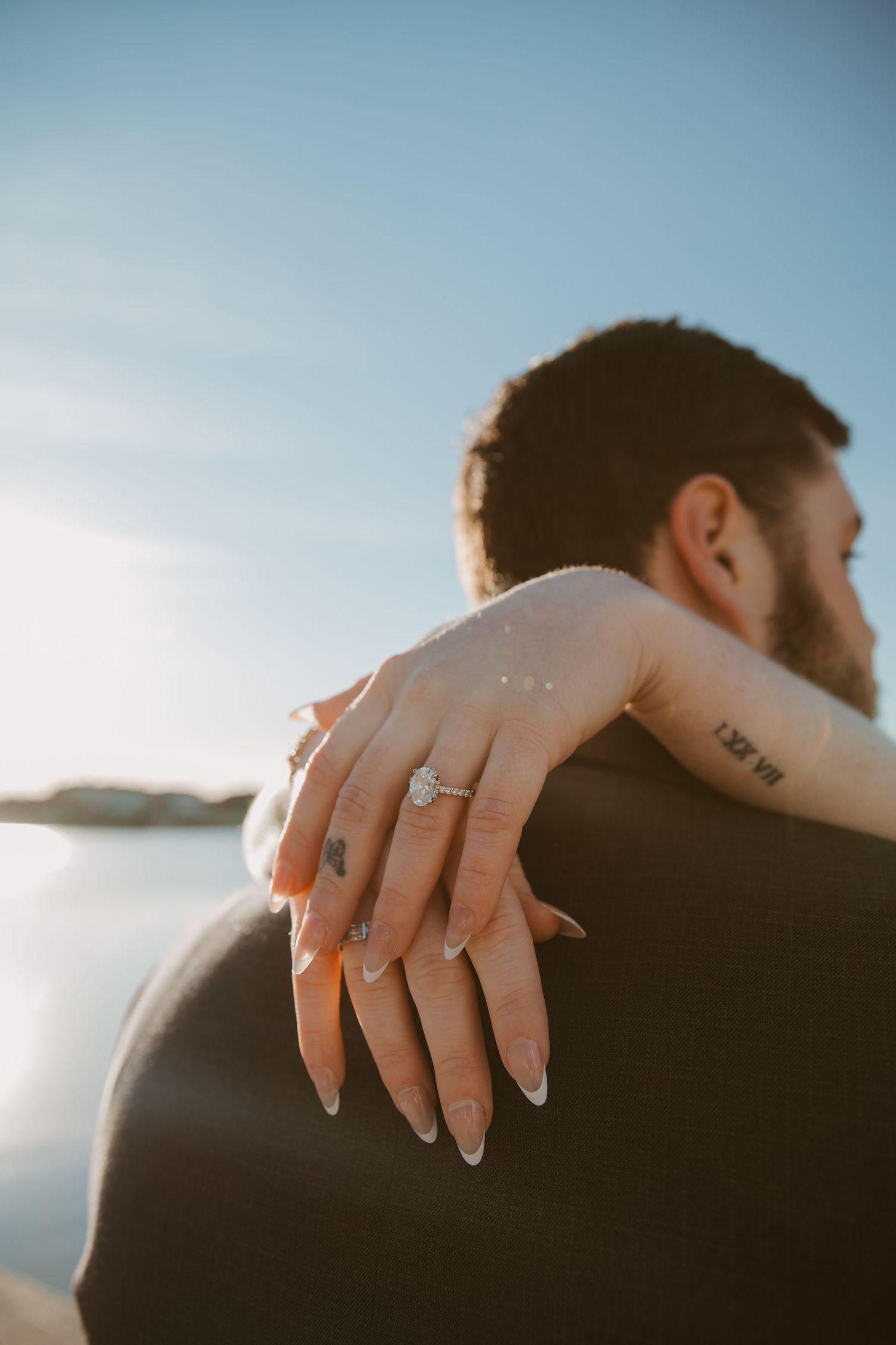 Close-up shot of hands with an engagement ring embracing against a seaside backdrop.