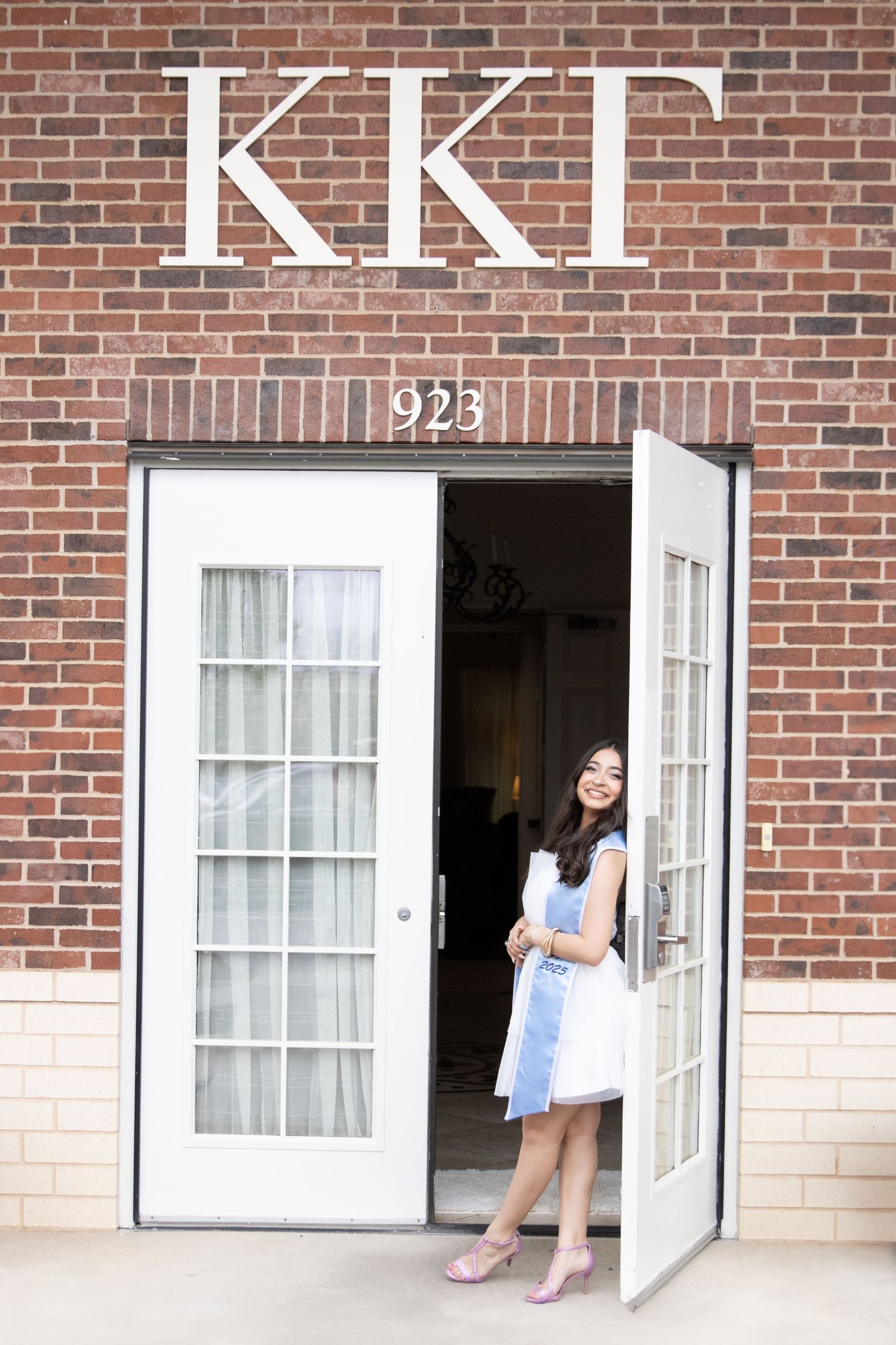 A brick building entrance with 'KKG' Greek letters and white French doors numbered 925.