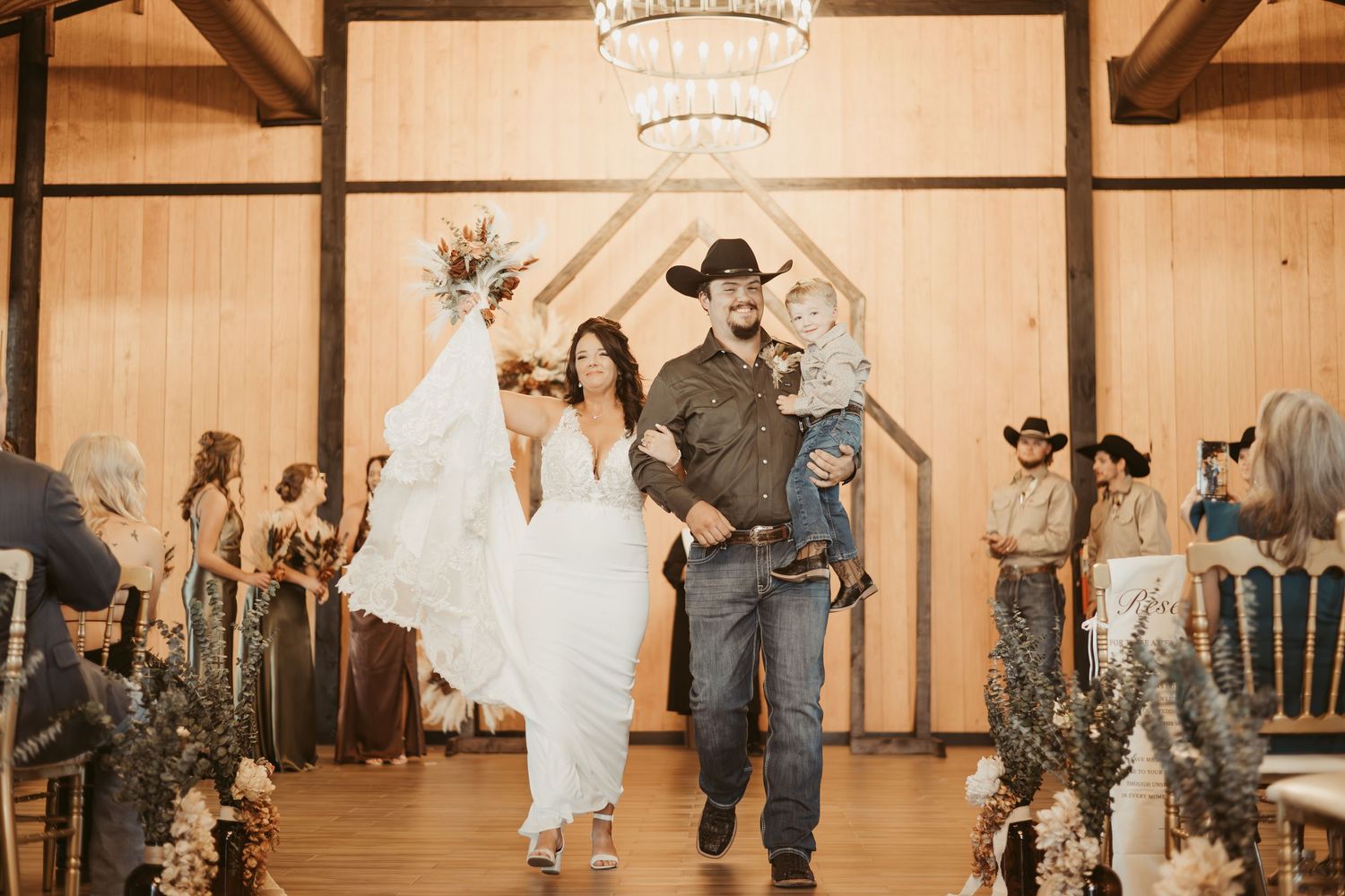 Couple dances together in rustic barn venue with wooden beams and chandeliers overhead during wedding reception. Wedding photographer DFW