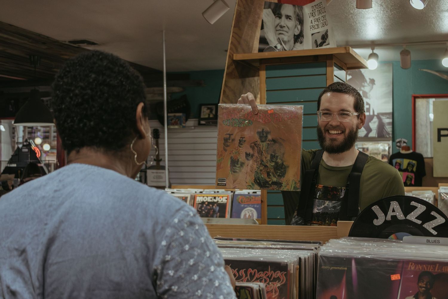 A customer interacts with a smiling jazz store clerk behind the counter in a music shop.