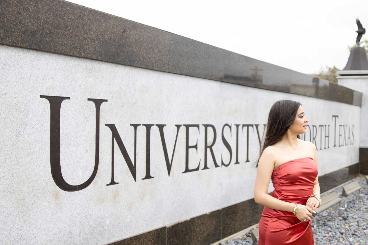 Red dress against university signage wall during golden hour.