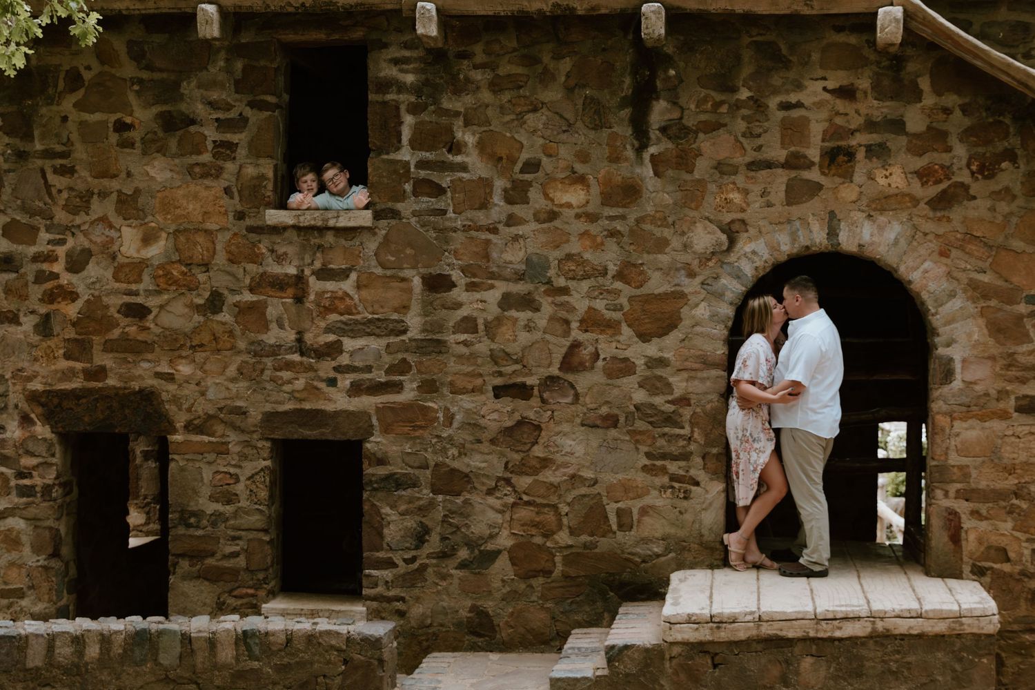 A couple stands embracing in a stone archway of an old rustic building during a romantic outdoor photography session.