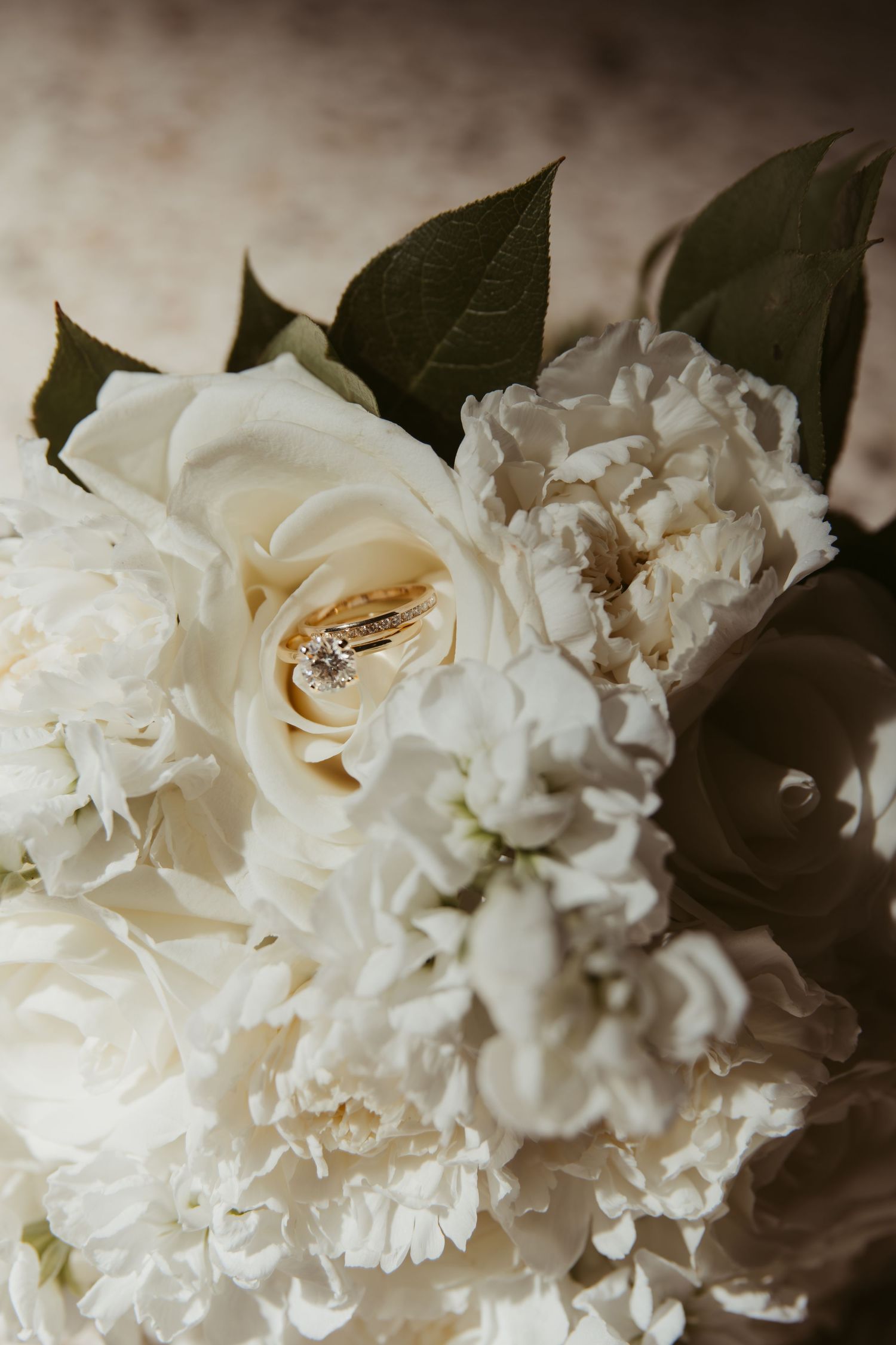 Close-up view of elegant white roses and carnations with dark green leaves against a moody background. Wedding Photographer DFW