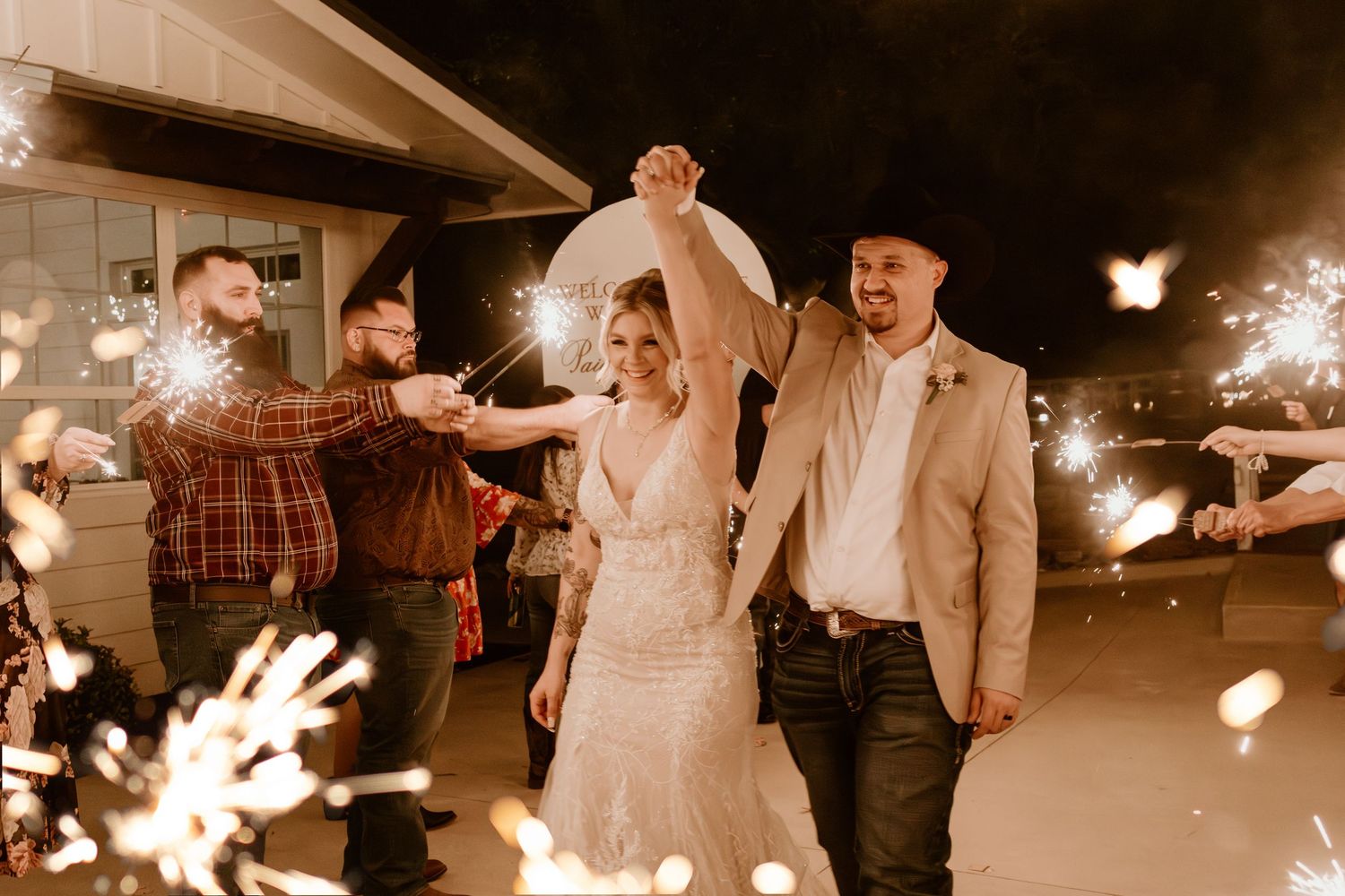 A wedding couple and guests dance joyfully at an evening reception with sparklers creating a magical atmosphere. Wedding Photographer DFW