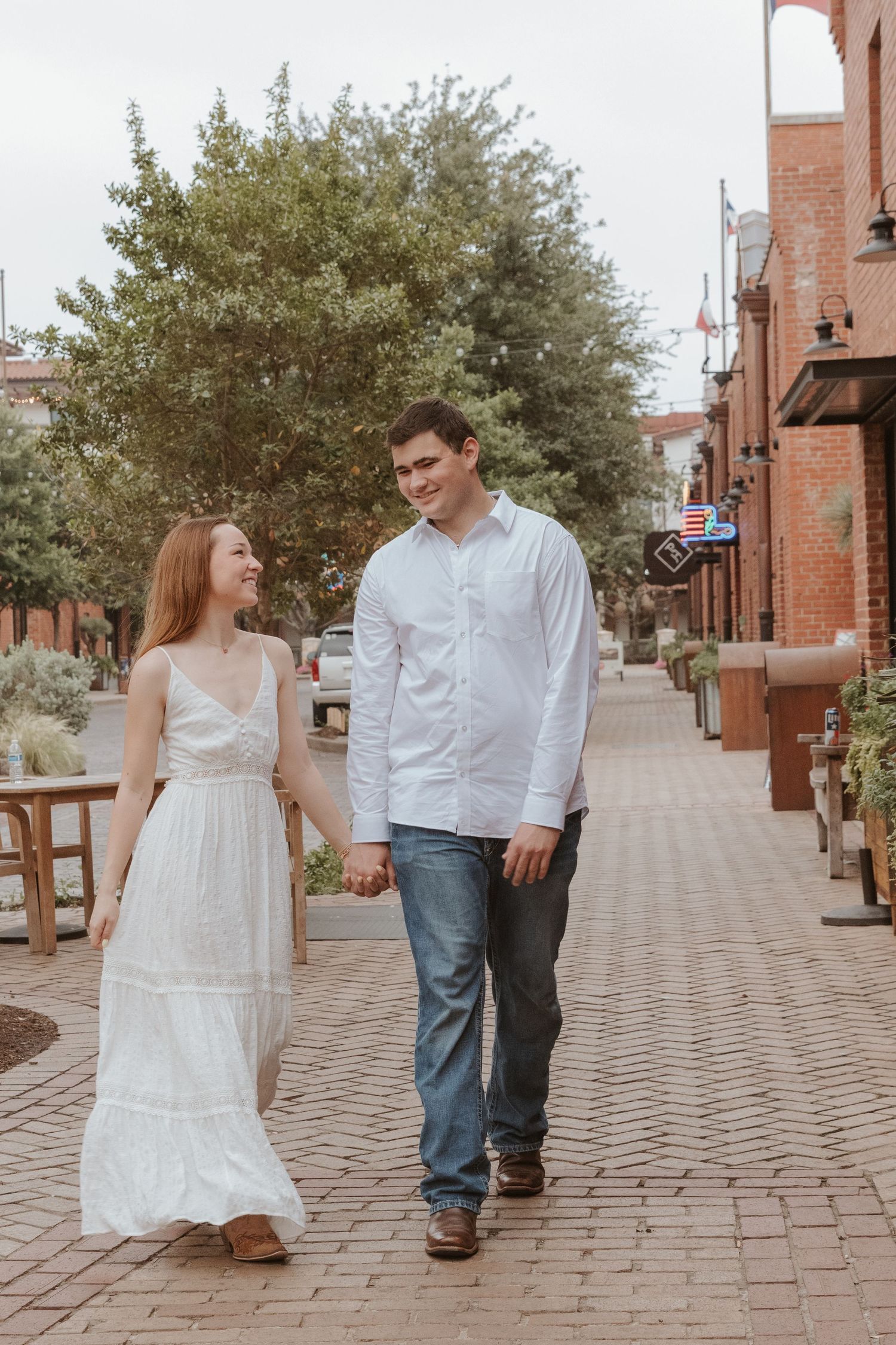 A couple walks hand in hand down a brick-paved street in a charming historic district on a sunny day.