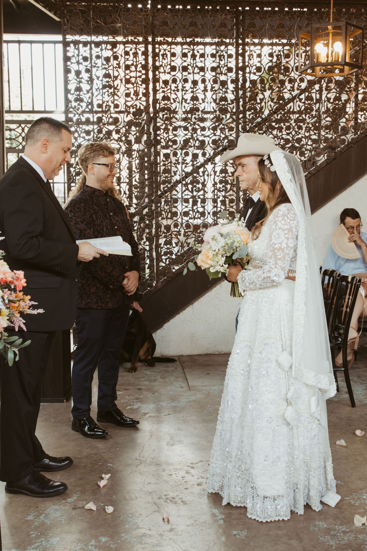 A wedding ceremony takes place in front of a sparkling curtain backdrop with an officiant and bride in lace gown.