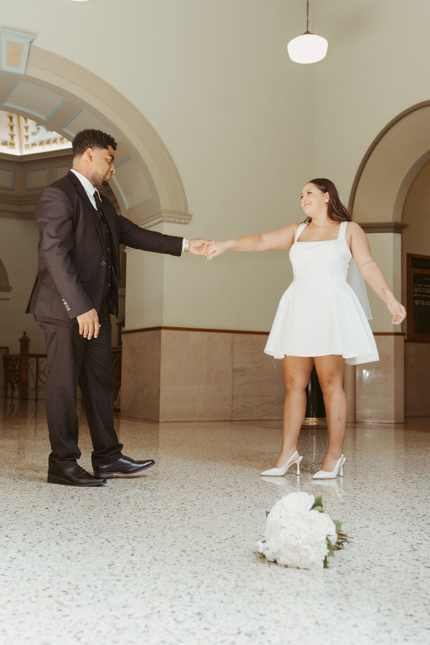 Couple in formal wear interacting playfully in an elegant indoor setting with arched ceilings. Wedding Photographer DFW