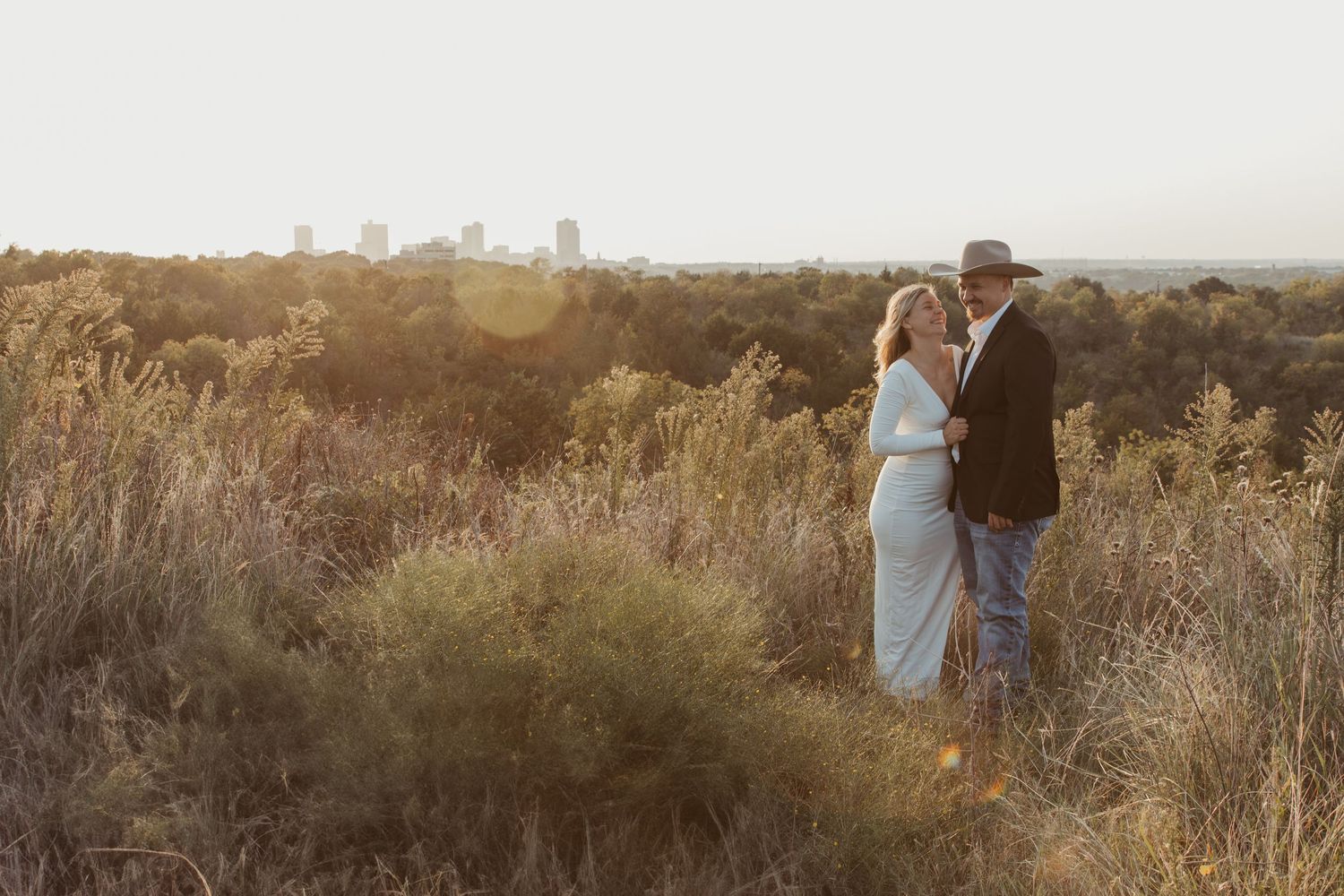 A couple walks through a golden field at sunset holding hands while exploring the autumn landscape. Engagement photographer DFW