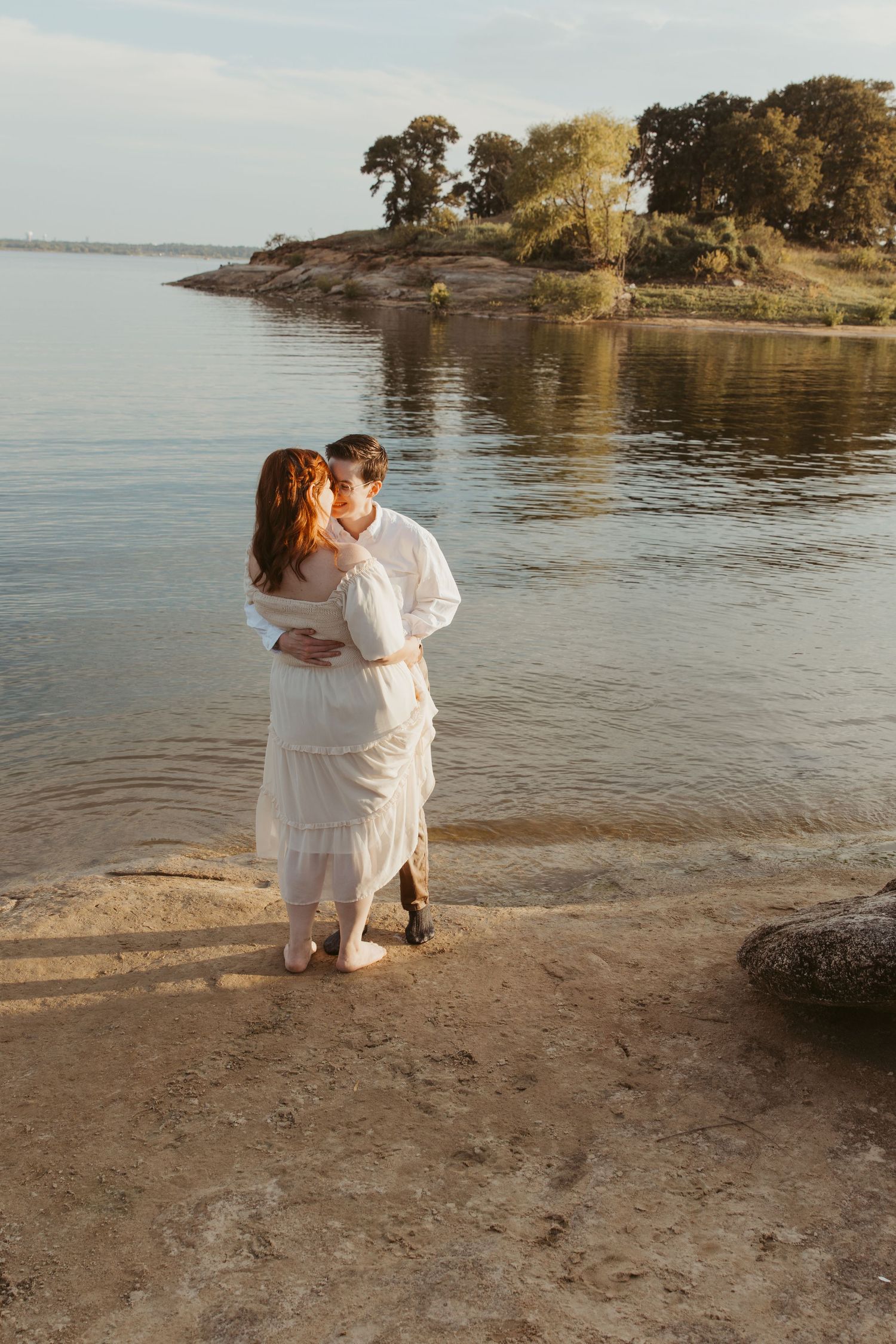 A romantic moment unfolds on a serene beach with golden sunlight illuminating the sandy shore and rocky coastline.