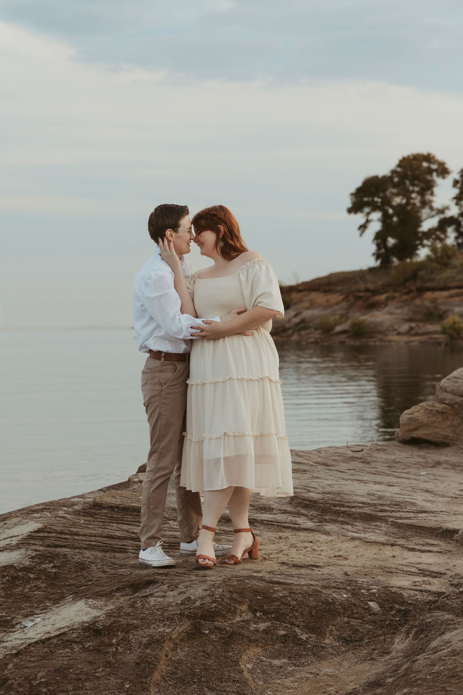 A couple shares a tender moment on rocky coastal outcrop during golden hour.