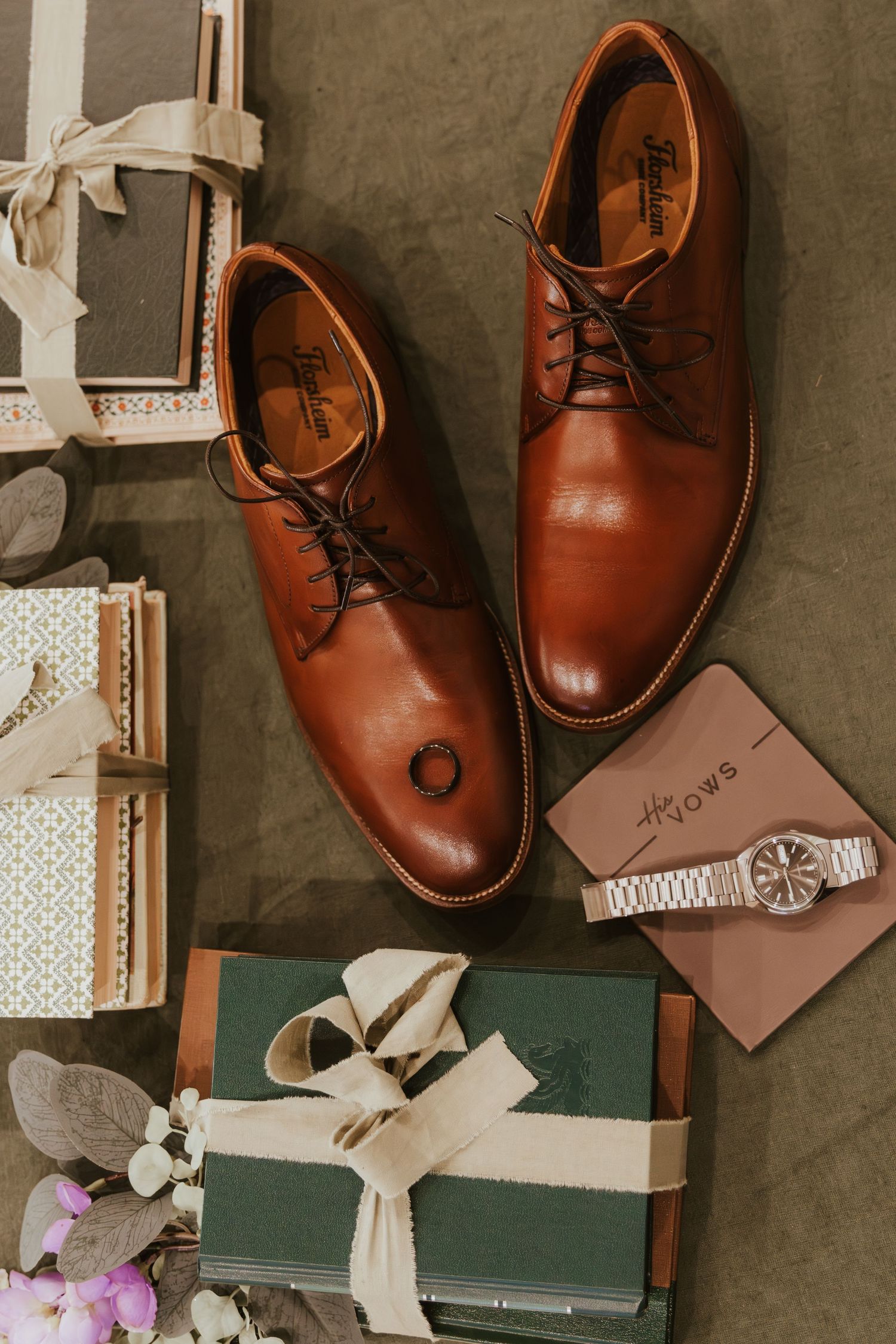 Brown leather dress shoes arranged with wrapped gifts, a watch, and decorative elements on a textured surface.