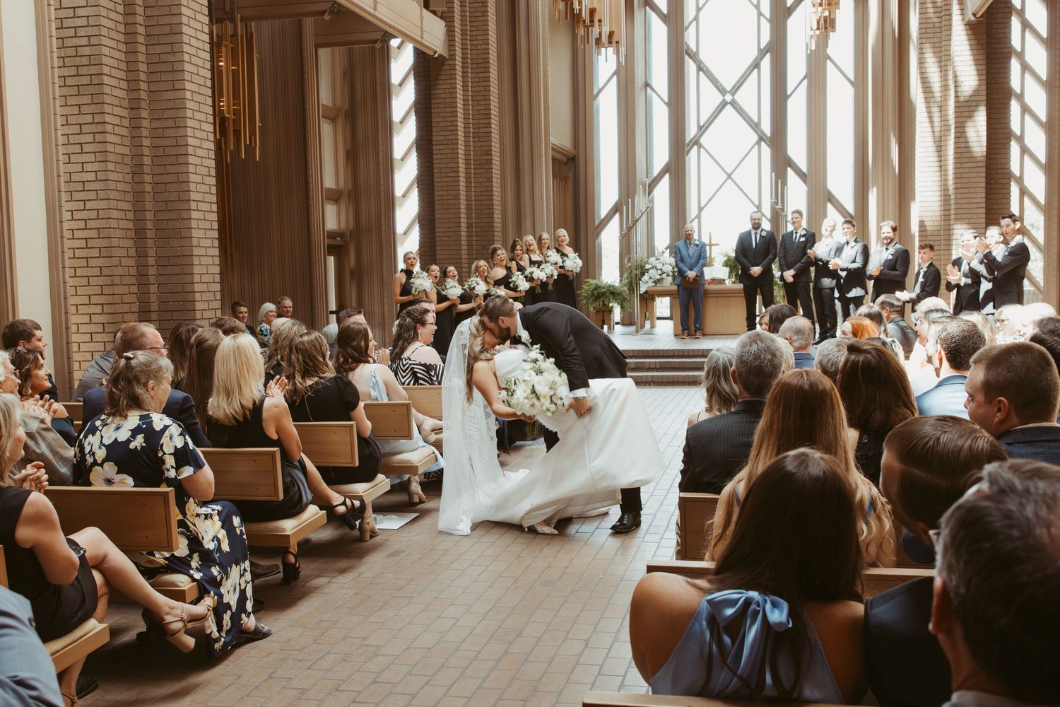 Couple shares a romantic dance during their wedding ceremony in an elegant chapel with guests looking on from wooden pews.