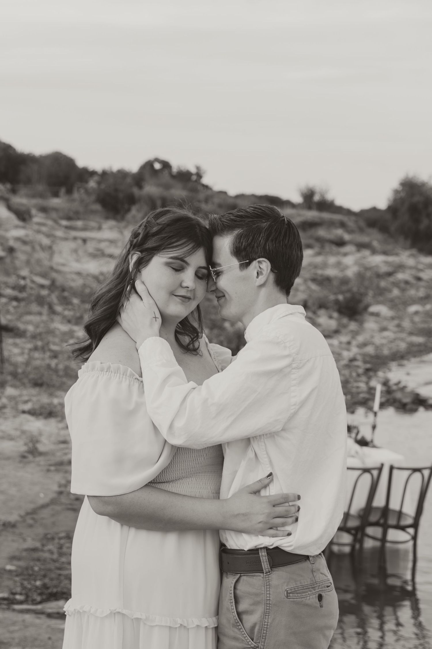 Black and white photo of couple in romantic embrace on rocky shoreline.