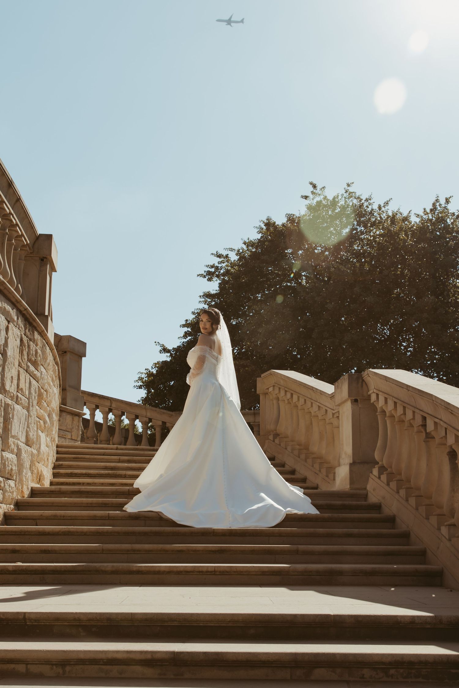Bride in flowing white ballgown twirls gracefully on ornate stone steps during sunset photo session.