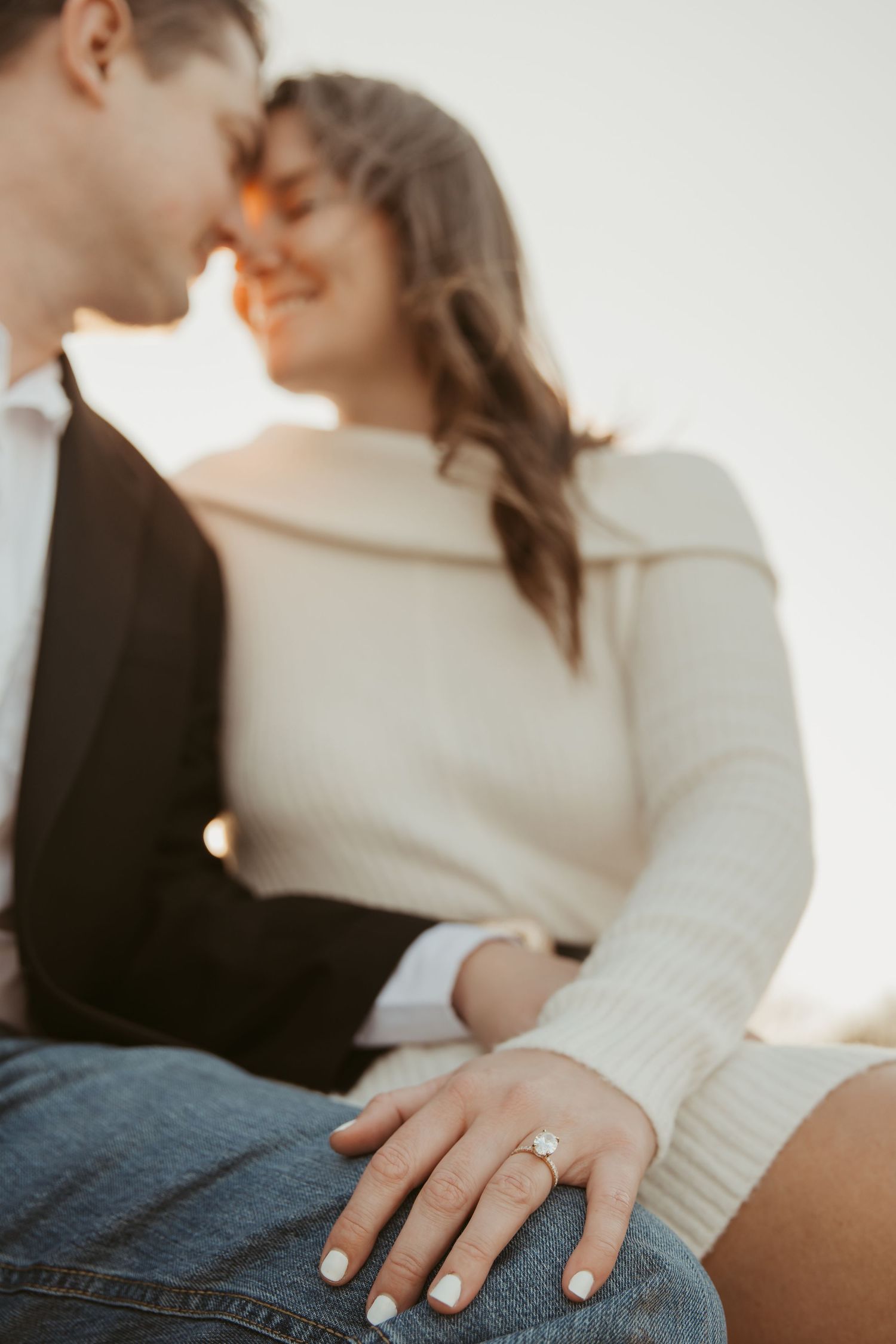 Smiling couple in romantic moment, woman displaying diamond engagement ring on hand resting on knee.