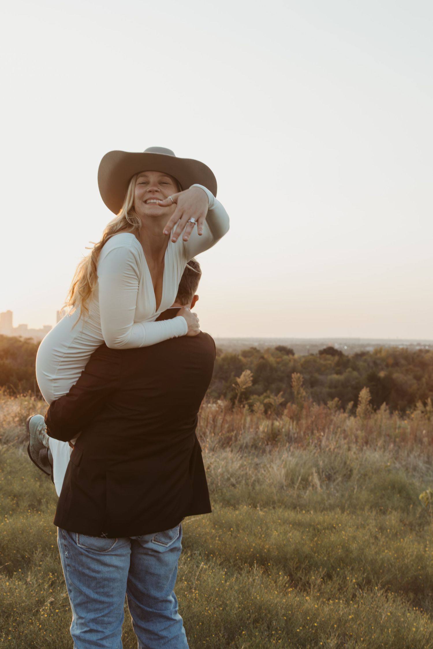 An affectionate couple shares tender moments in a sunlit meadow while wearing country western clothing.