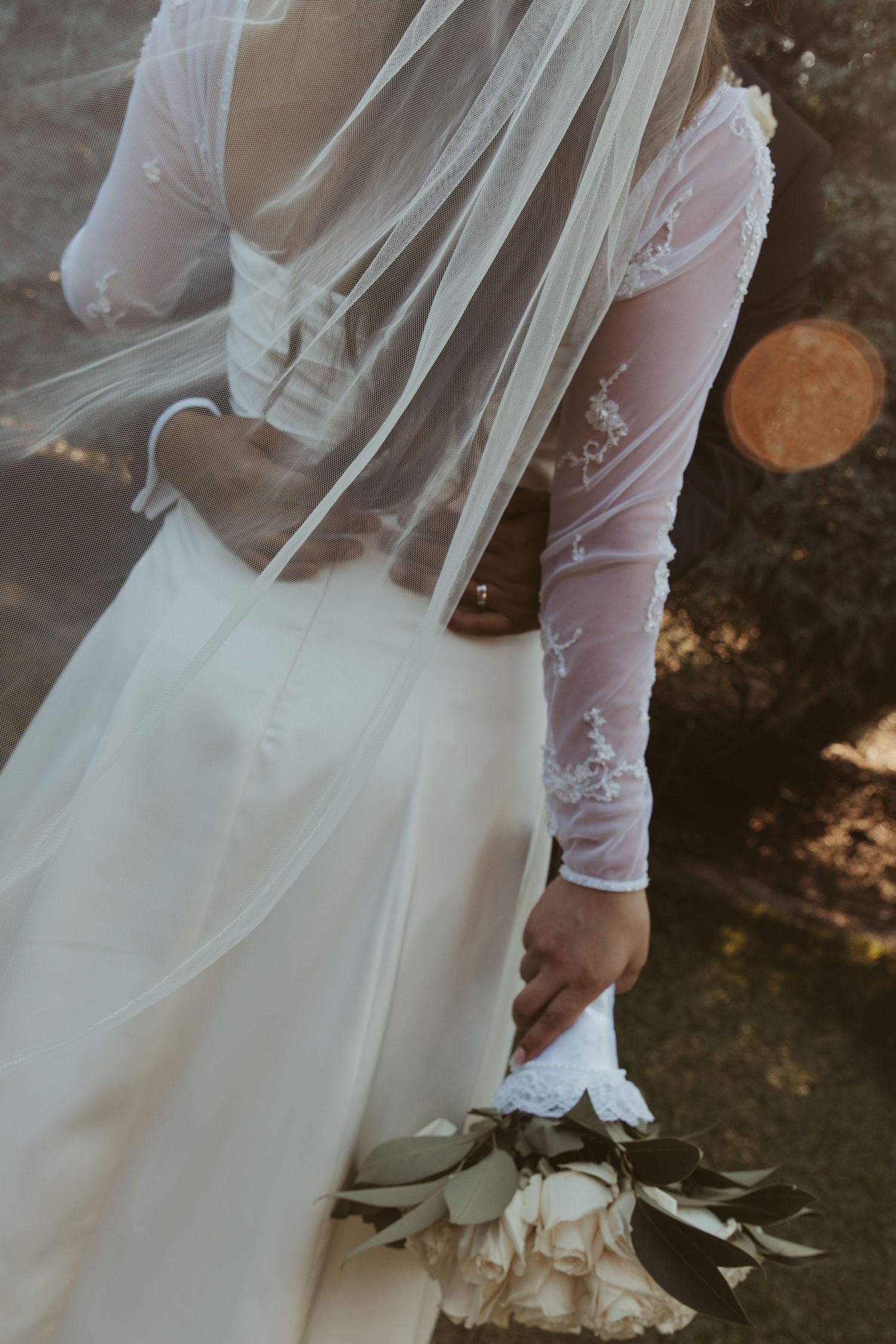 A close-up view of a white wedding dress with lace details and flowing fabric in natural lighting.
