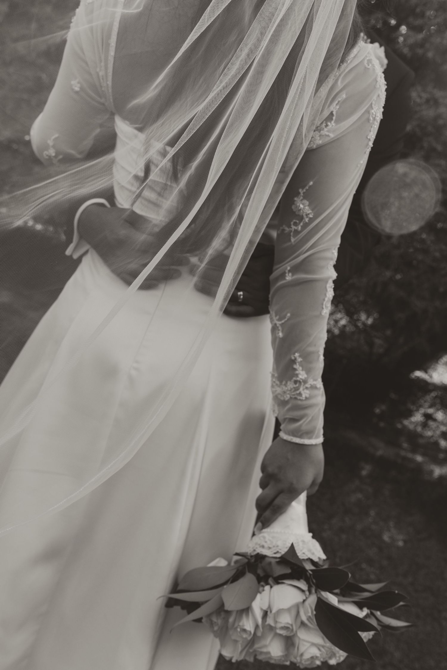 Black and white detail shots of elegant wedding dress with lace sleeves and flowing tulle skirt from various angles.