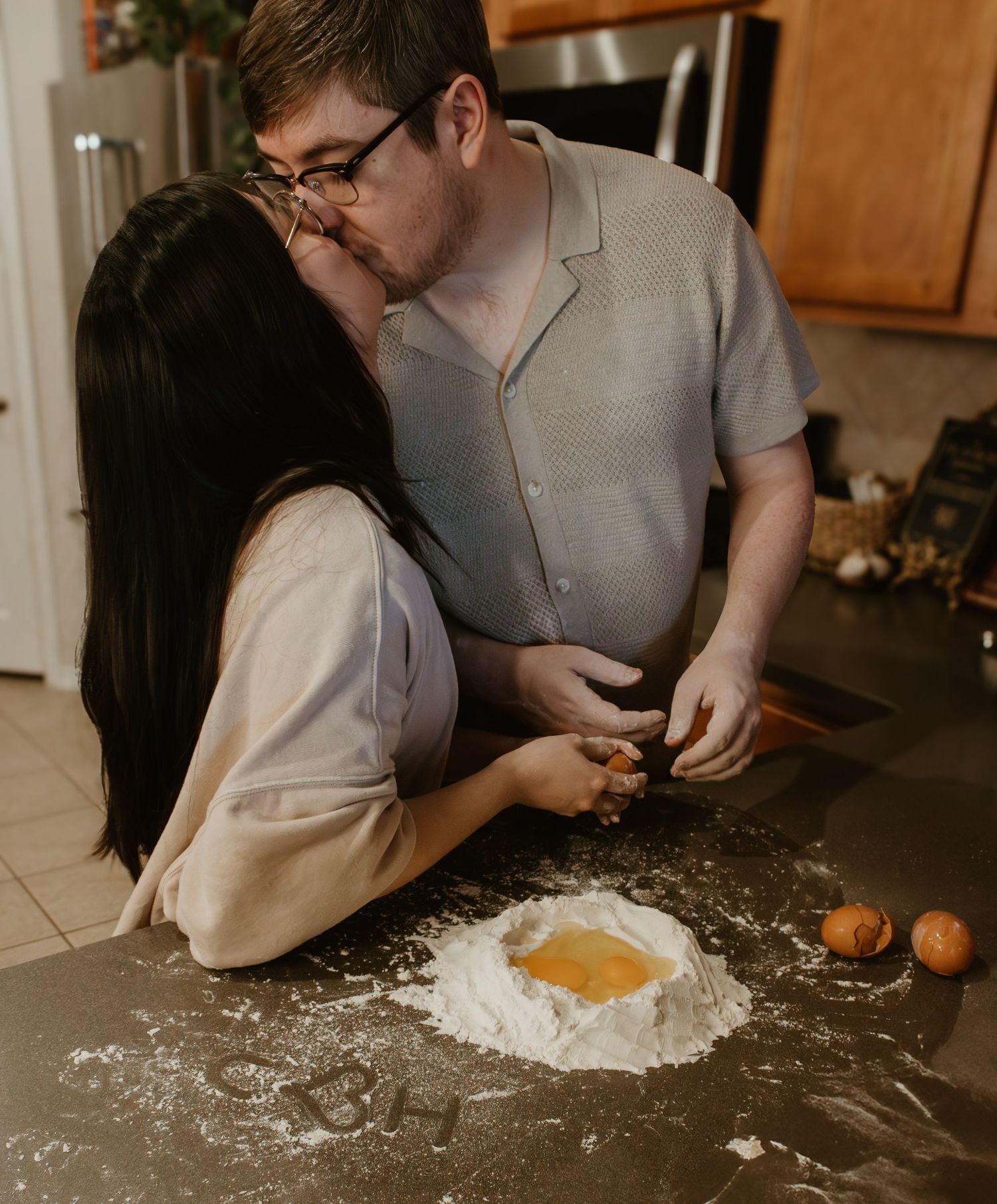 A couple making pasta dough from scratch with flour and eggs on their kitchen counter.