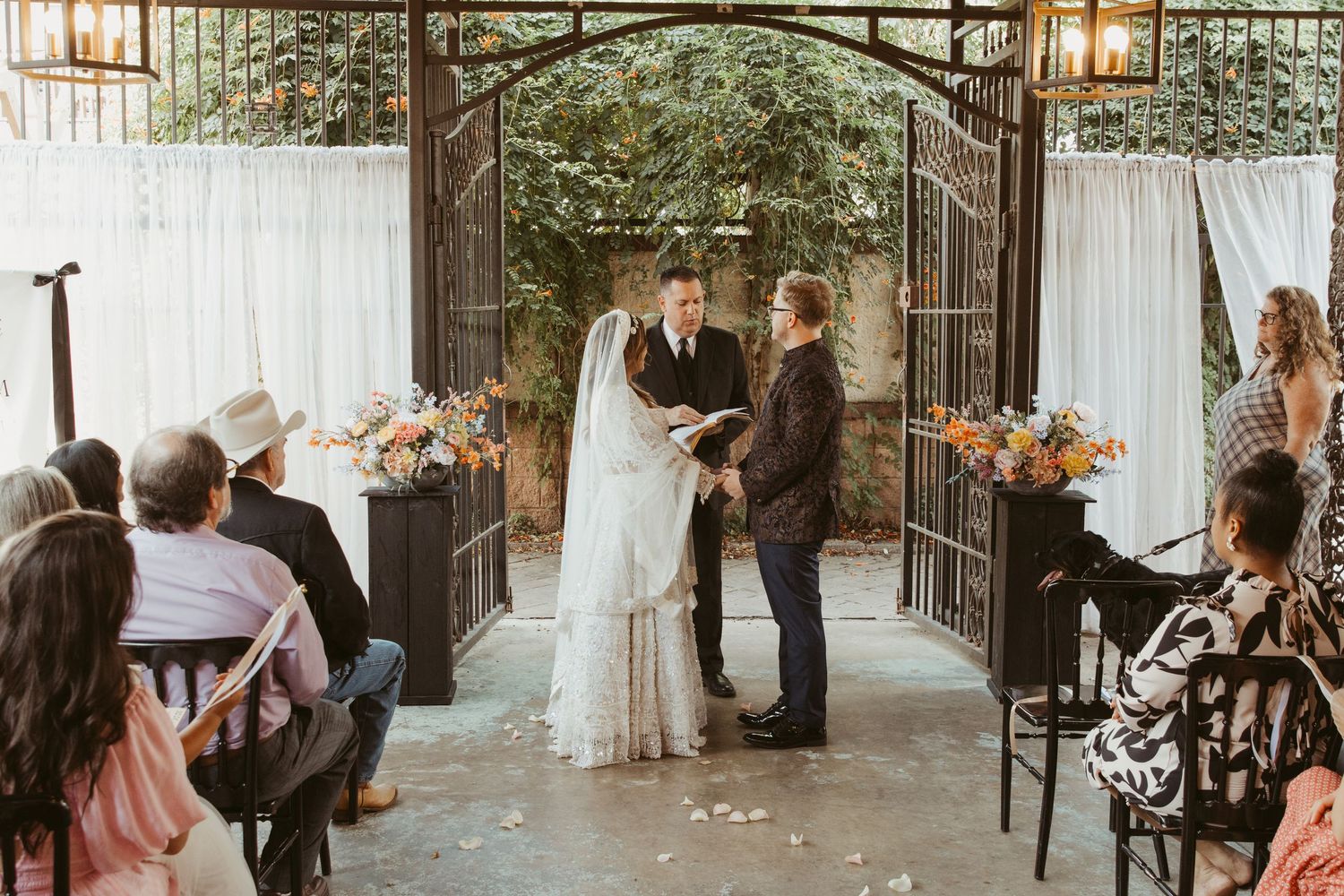 Intimate outdoor wedding ceremony under an iron archway with guests seated on either side.