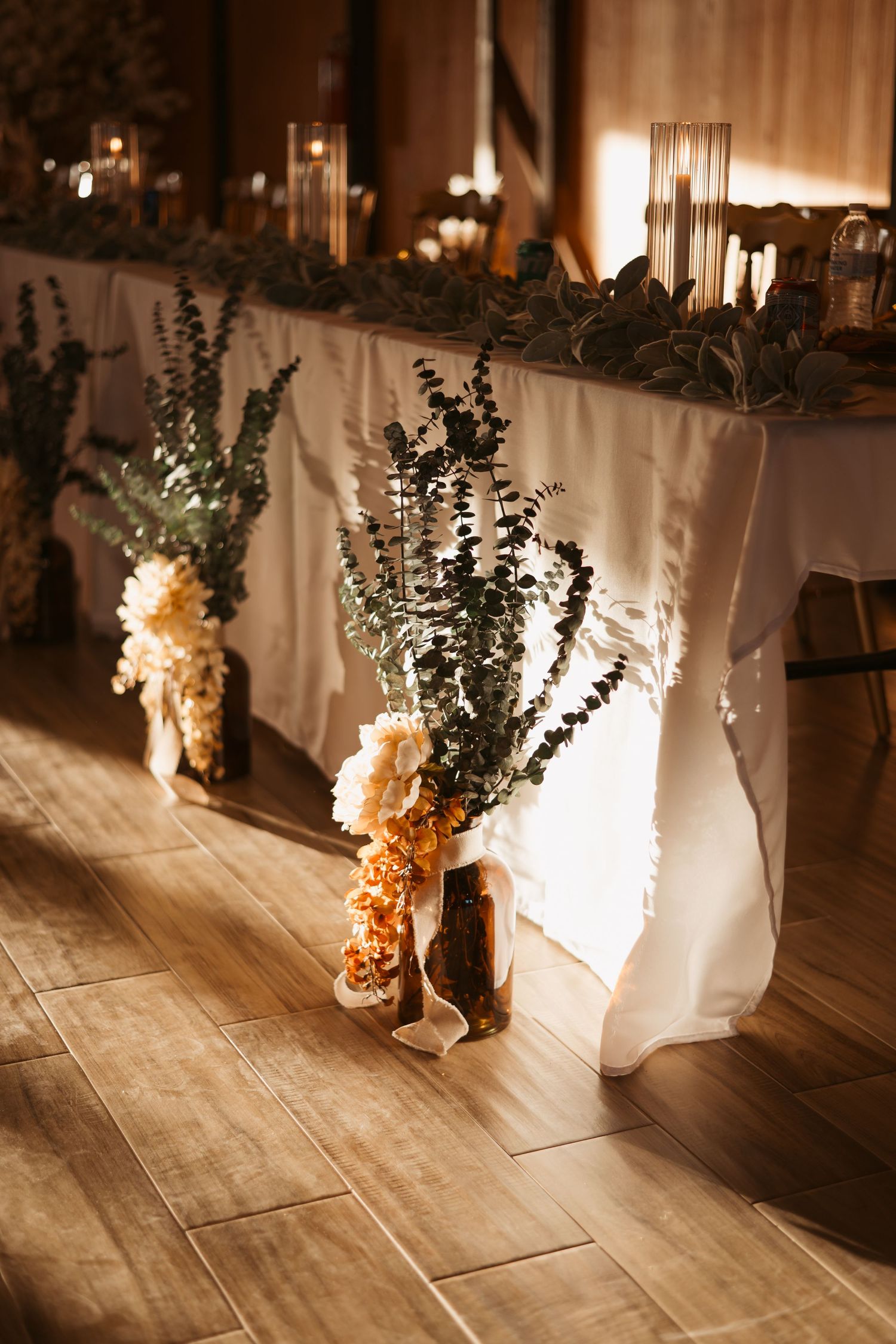 White tablecloths drape elegantly over tables with floral arrangements creating a romantic wedding reception atmosphere. Wedding photographe