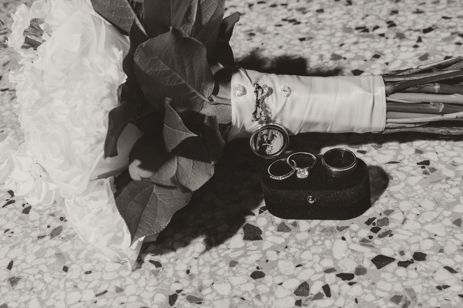 A black and white photograph shows scattered roses and a wine bottle lying on a textured surface.