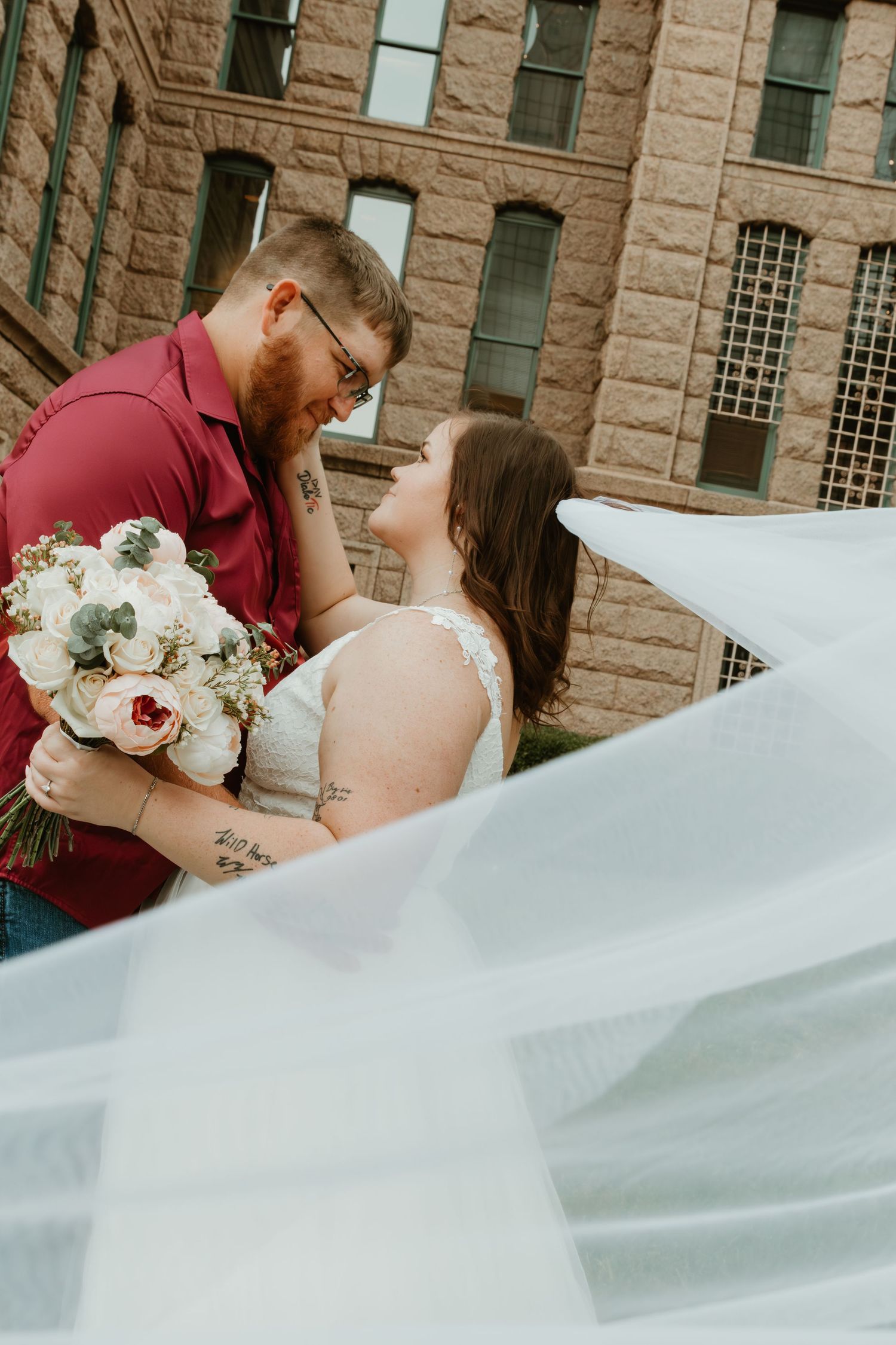 A romantic wedding portrait against historic stone architecture with flowing veil in foreground.