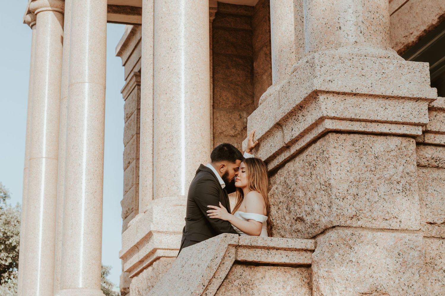 Couple sharing an intimate moment between classic stone pillars of an elegant architectural setting during golden hour.