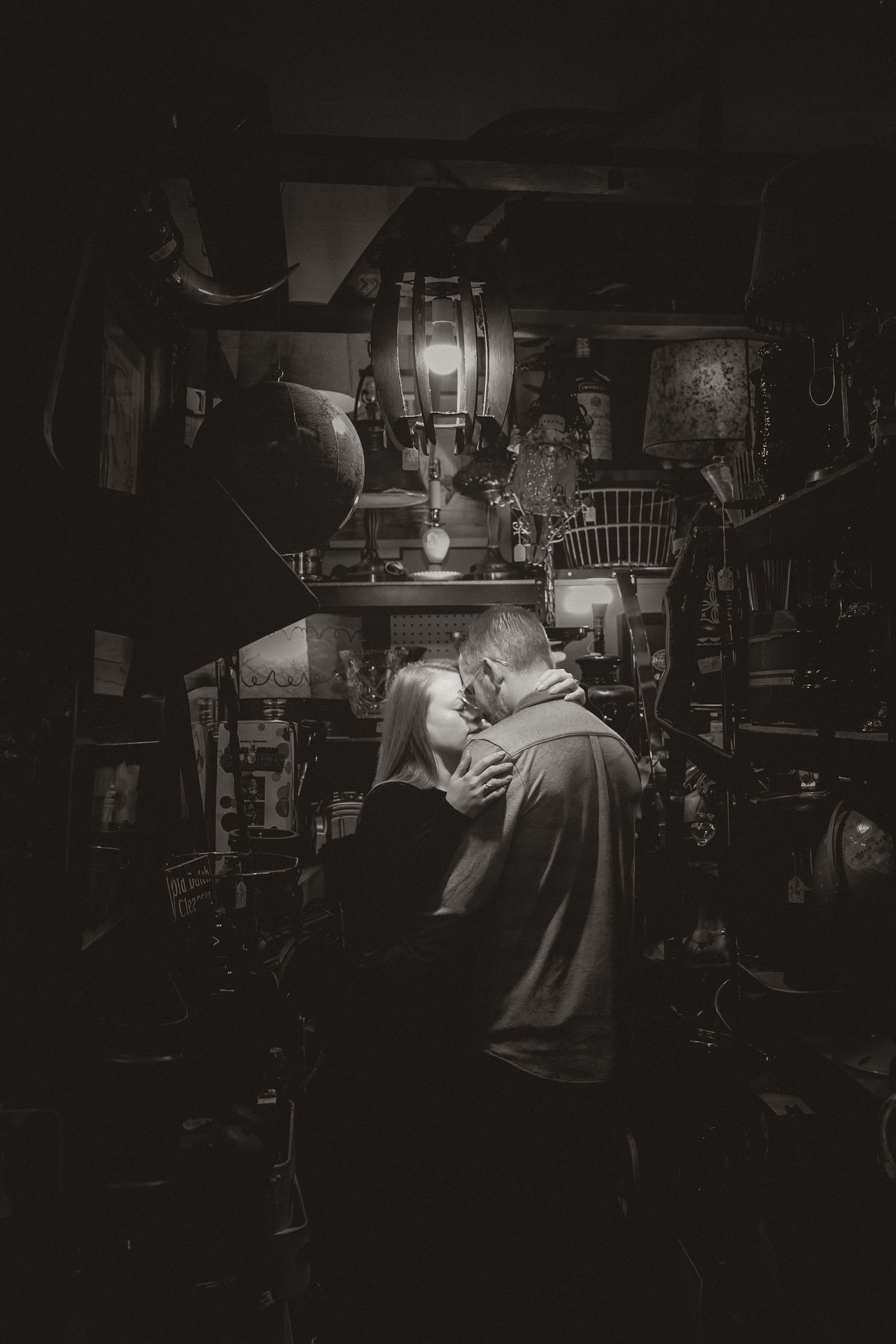 A black and white photograph showing a movie projector operator working in a dark projection booth with vintage equipment.