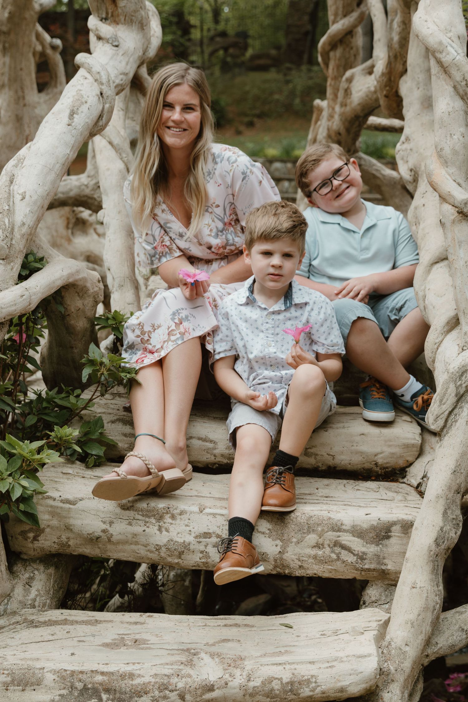 A family photo taken on rustic wooden steps surrounded by natural driftwood sculptures.