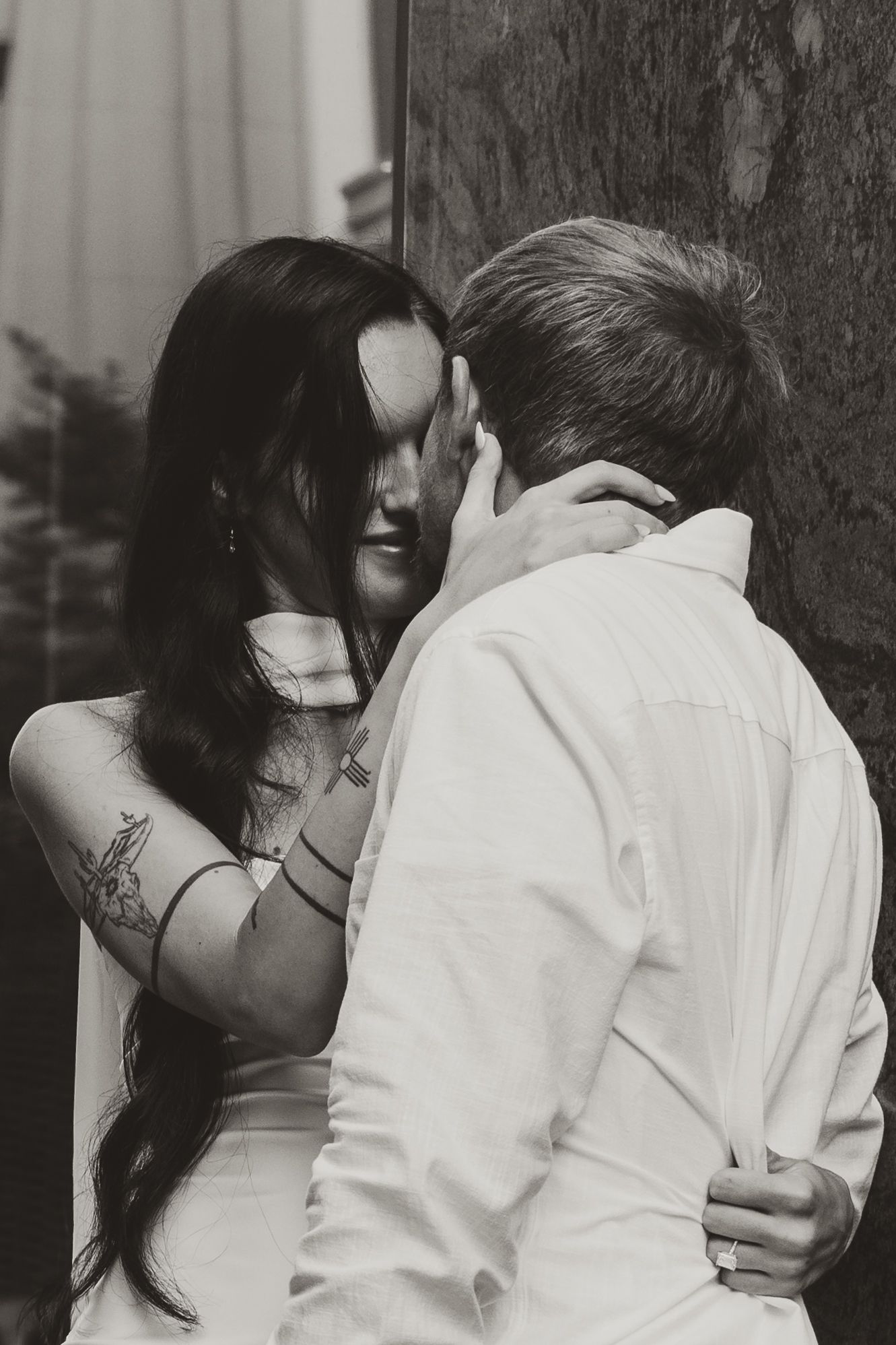 Black and white romantic portrait of a couple embracing intimately against a wall in artistic lighting.