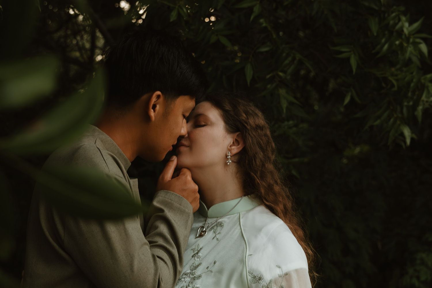 Romantic couple shares tender moment among garden foliage.