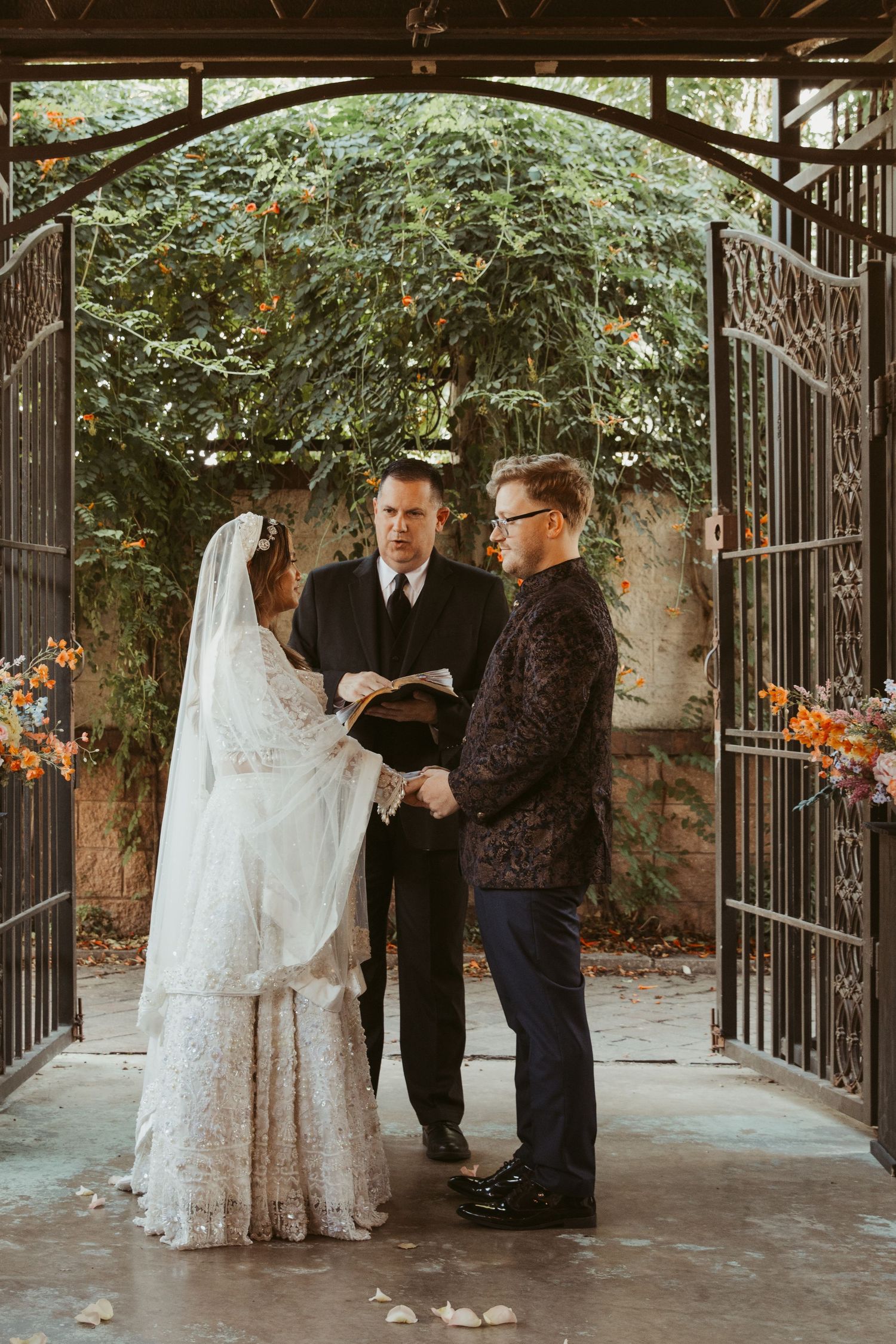 Romantic outdoor wedding ceremony under an iron archway decorated with greenery.