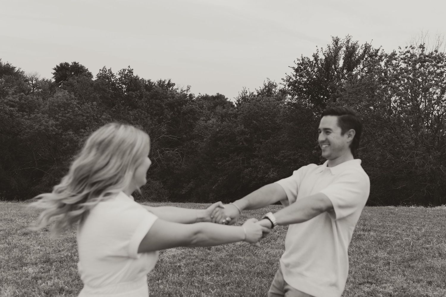 A black and white sequence of photos showing a playful couple spinning around in a field at sunset.