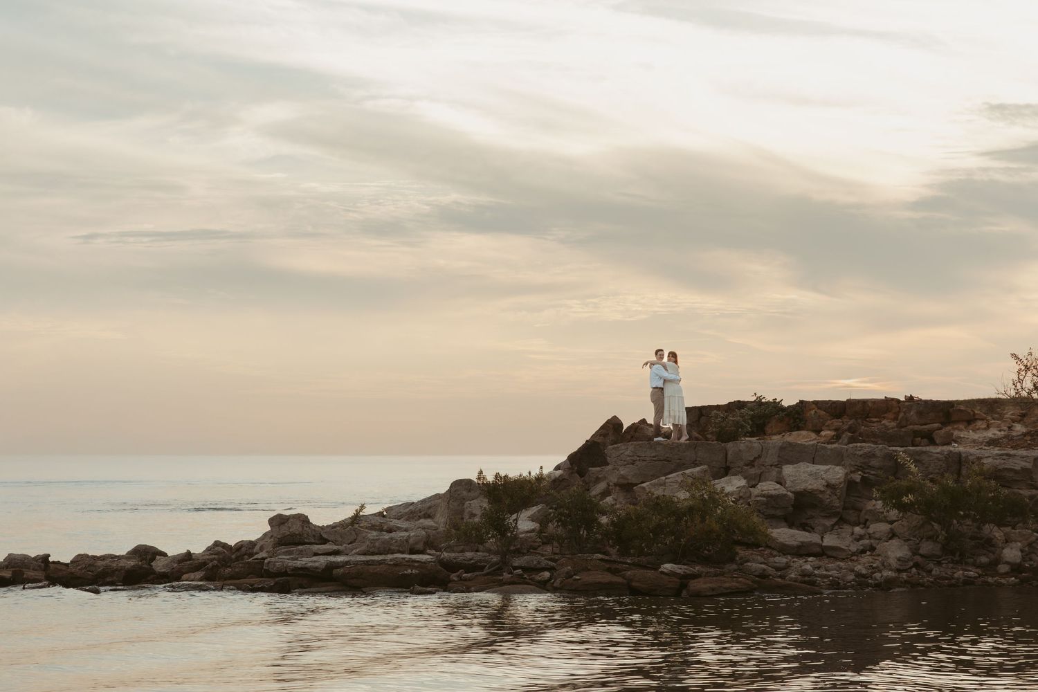 Panoramic view of a lighthouse on rocky coastline during golden hour with cloudy sky.